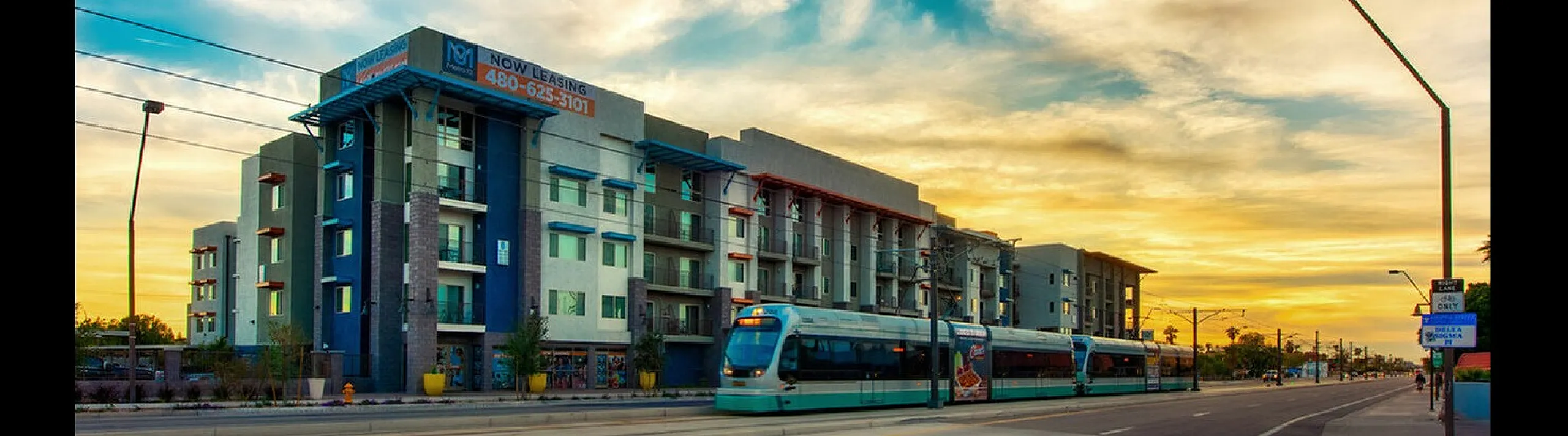 Vibrant apartment building with modern architecture against a stunning sunset sky, featuring convenient access to public tram services.