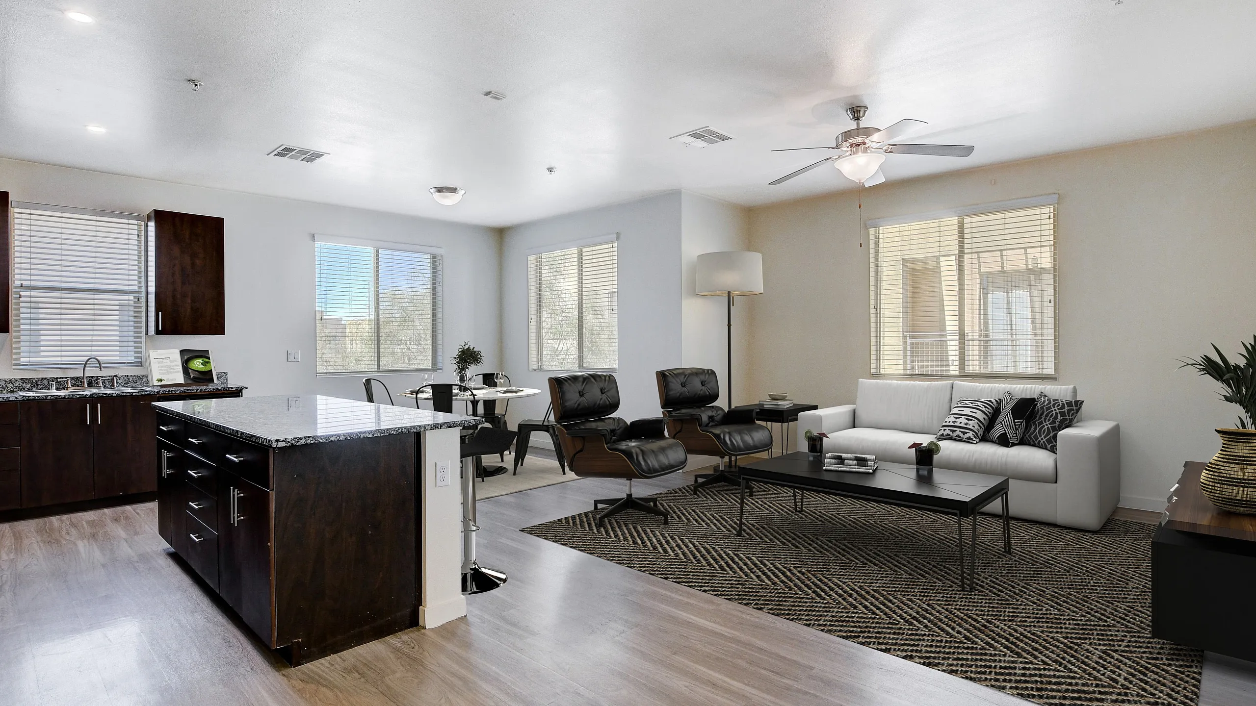 Modern open-floor living room and kitchen with sleek hardwood floors, stylish furnishings, and abundant natural light.