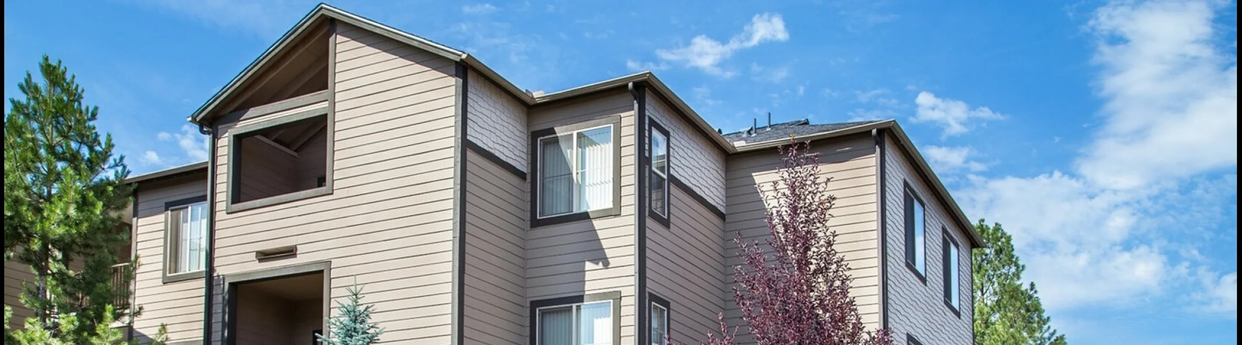 Charming exterior view of The Lodge Luxury Apartment Homes, surrounded by lush greenery and vibrant landscapes, offering serene living in a prime location.