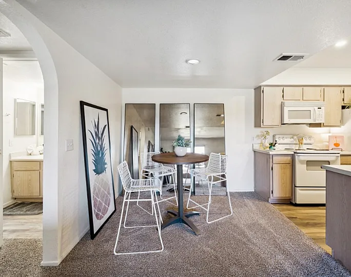 Bright and cozy dining area with modern white chairs and a wooden table, adjacent to a sleek kitchen featuring light wood cabinets and appliances, ideal for comfortable living.