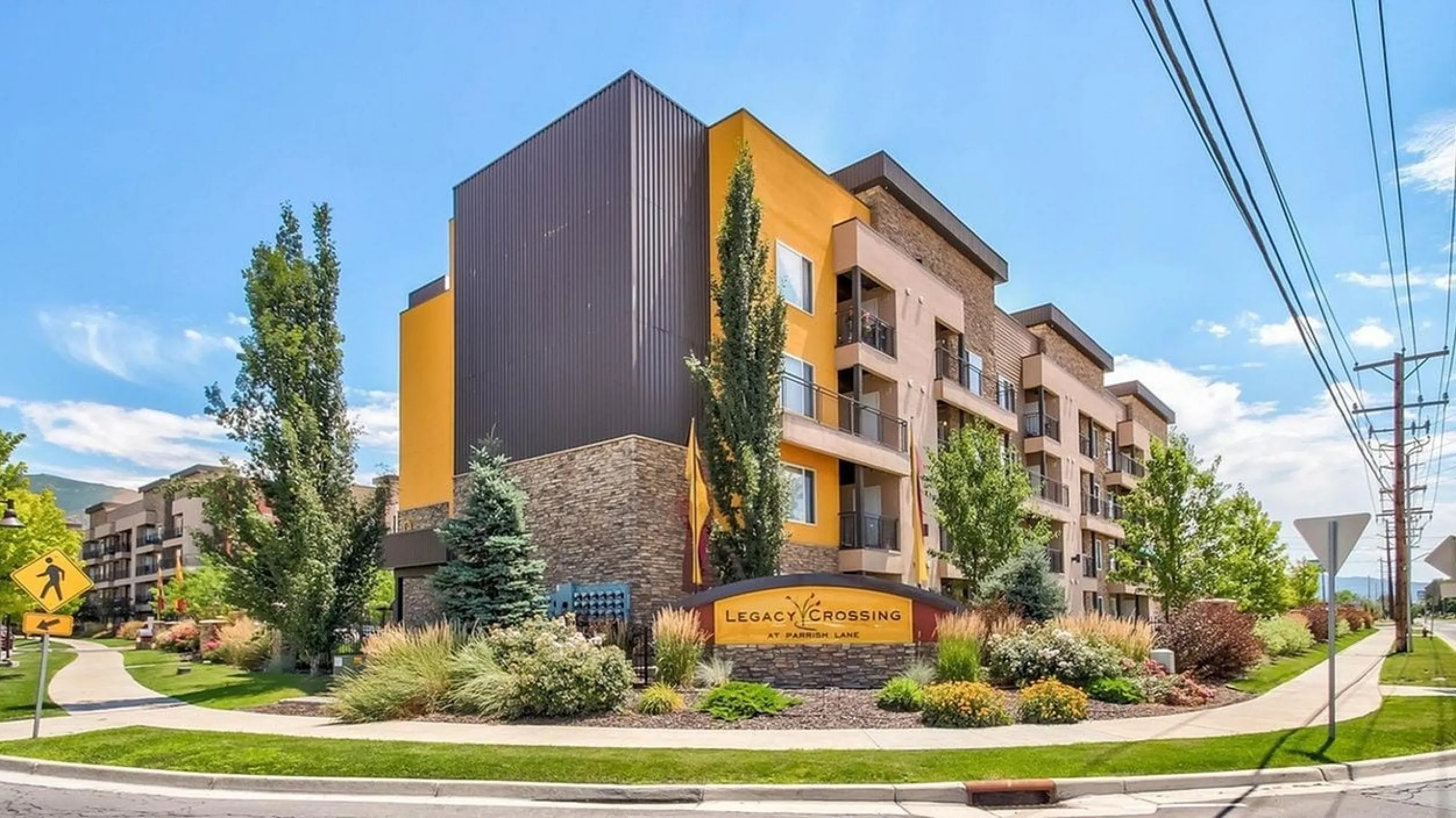 Contemporary apartment building at Legacy Crossing with stylish architecture, lush landscaping, and vibrant greenery under a bright blue sky.