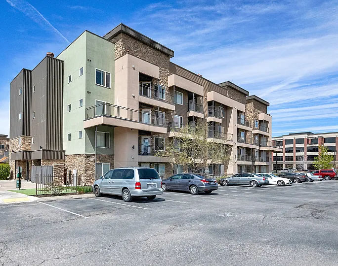 Modern apartment complex with stylish architecture, featuring spacious balconies and ample parking, under a bright blue sky.