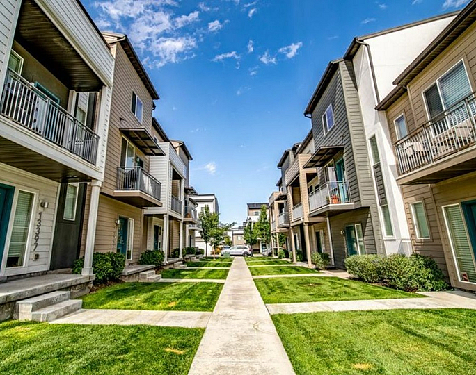 Charming modern apartment complex with balconies, lush green surroundings, and a bright blue sky.