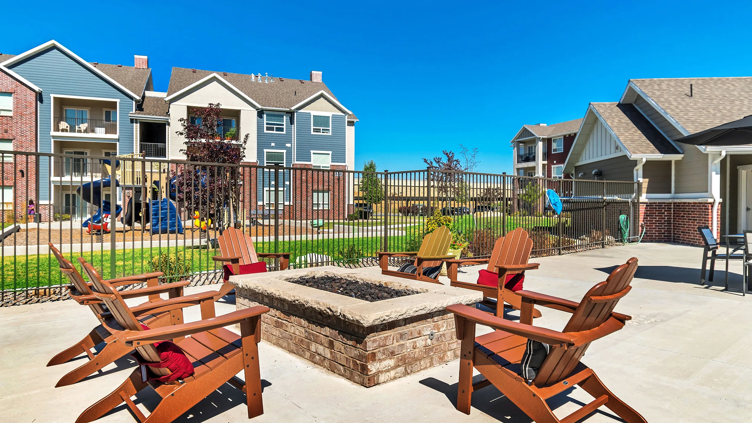 Inviting outdoor space with cozy Adirondack chairs around a brick fire pit, perfect for relaxing and enjoying the vibrant community atmosphere.