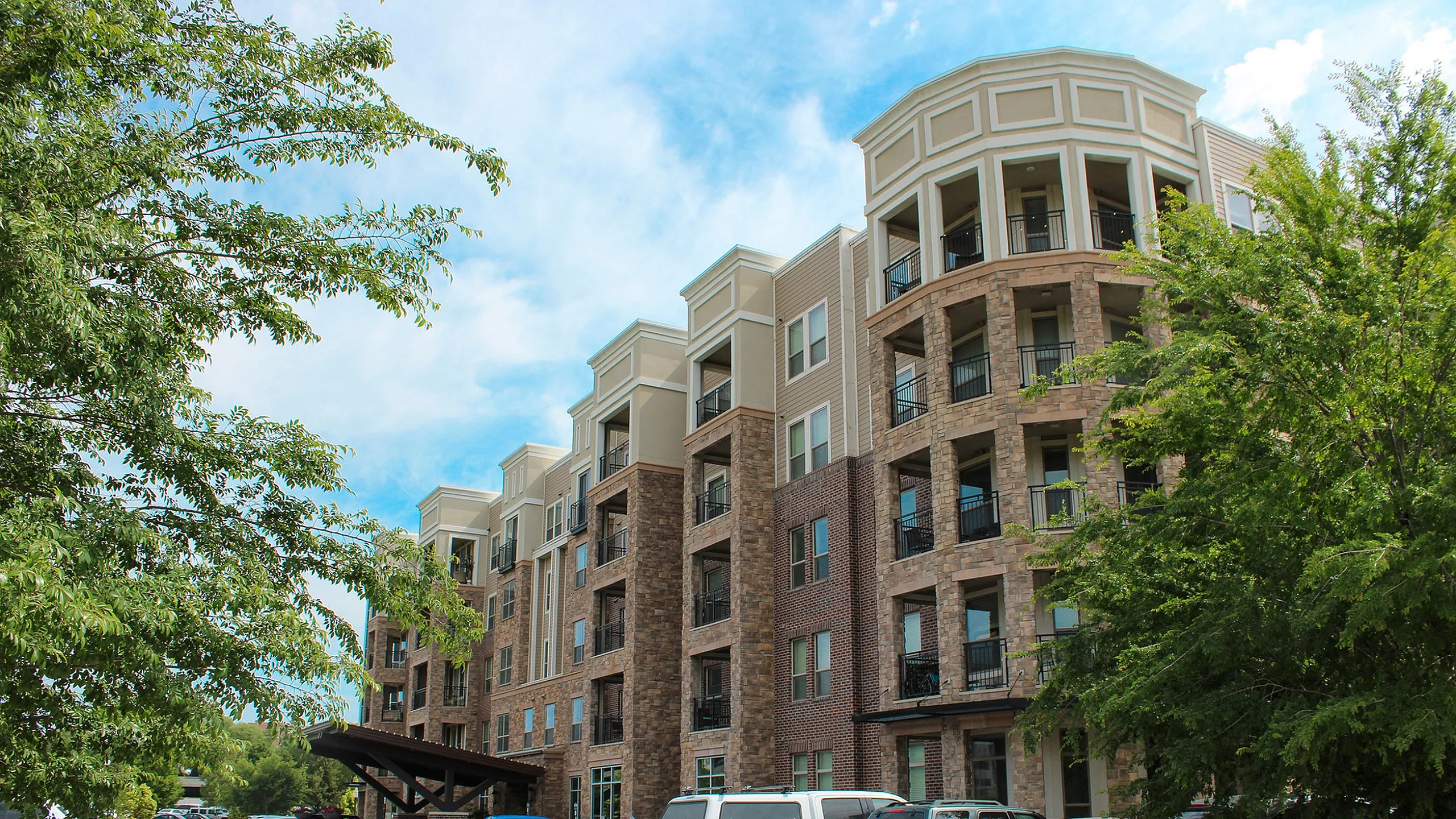 Modern apartment building with stylish balconies, surrounded by lush greenery and ample parking.