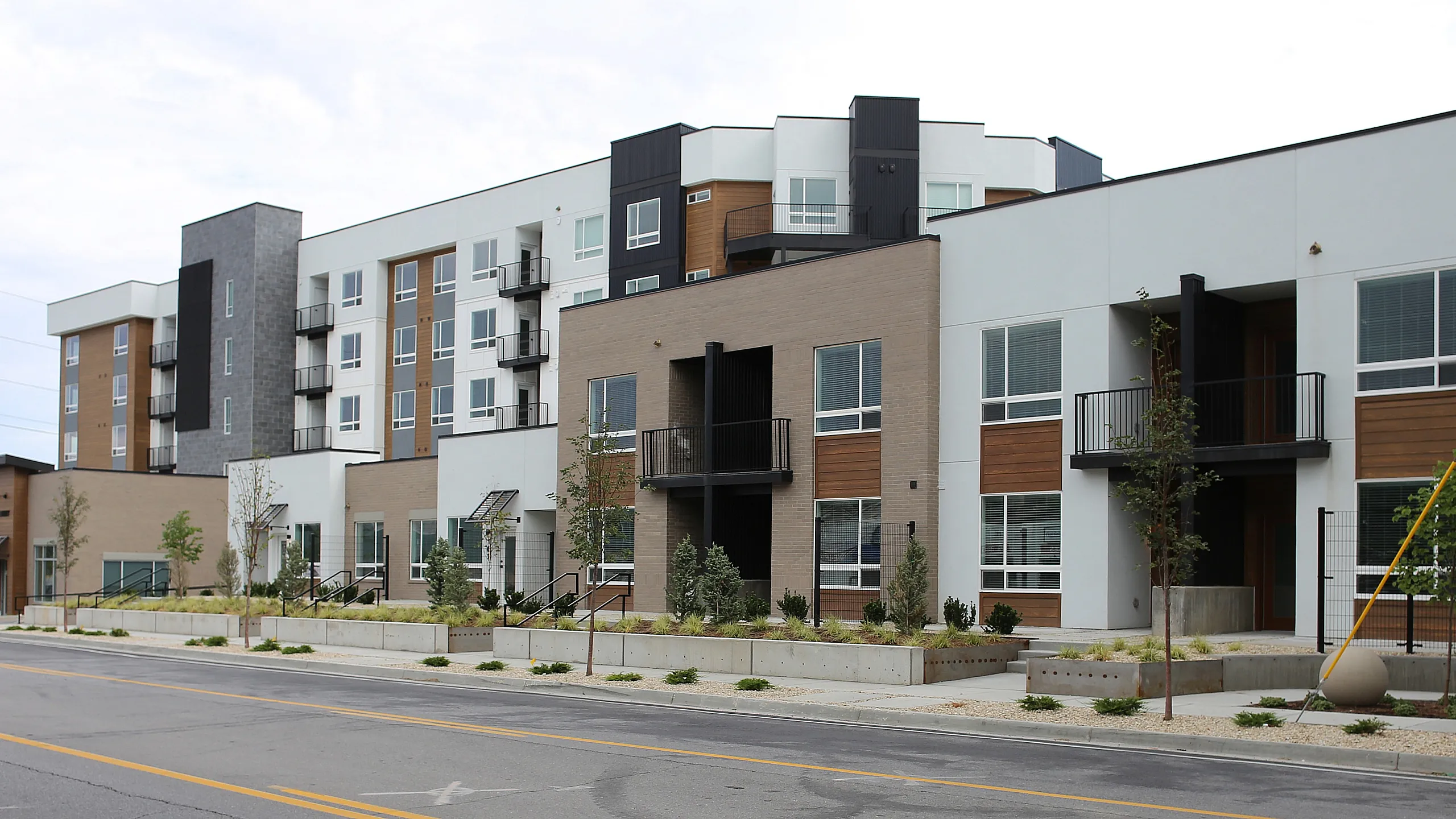 Modern apartment complex featuring sleek architecture with large windows, balconies, and a landscaped entrance.