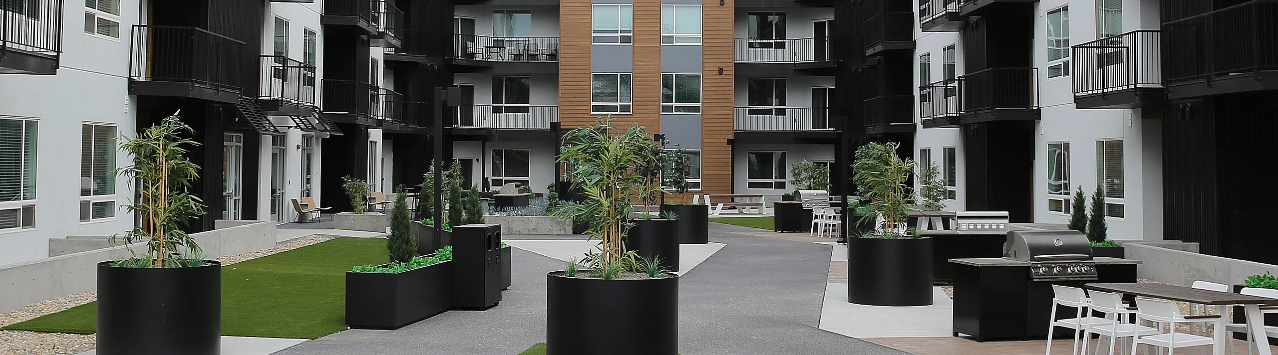 Modern apartment complex courtyard with stylish black balconies and lush green landscaping, ideal for relaxation and socializing.