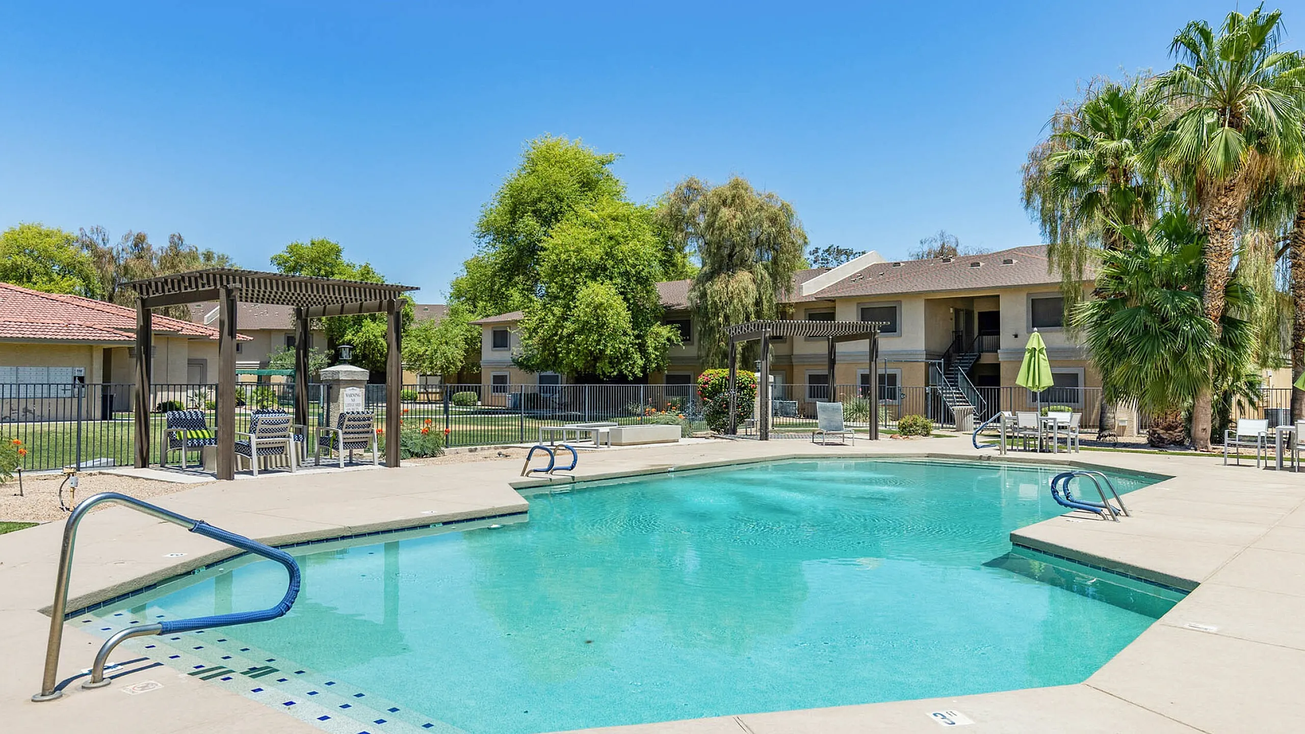 Inviting apartment complex with a sparkling swimming pool surrounded by lush greenery and comfortable seating under stylish pergolas.