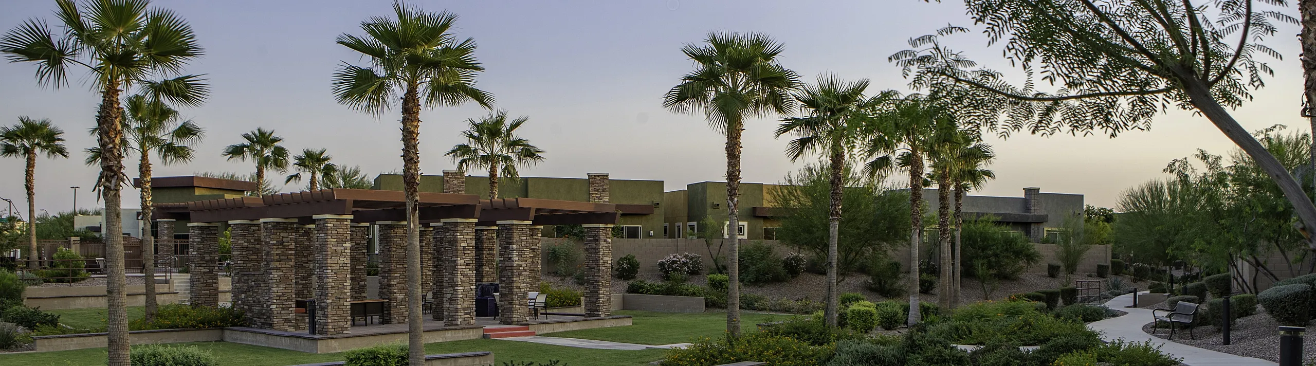 Charming community garden path lined with palm trees, featuring stylish pergolas and lush landscaping.