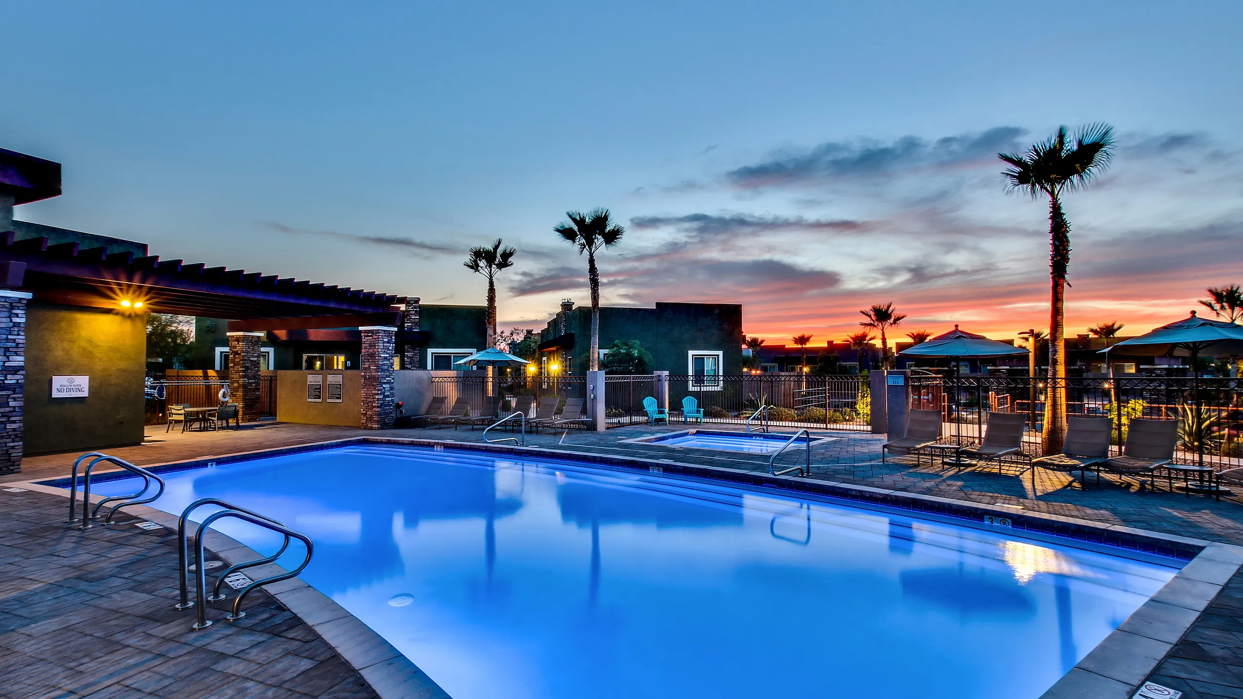 Luxurious pool area at sunset featuring modern lounge chairs, palm trees, and ambient lighting for a serene living experience.