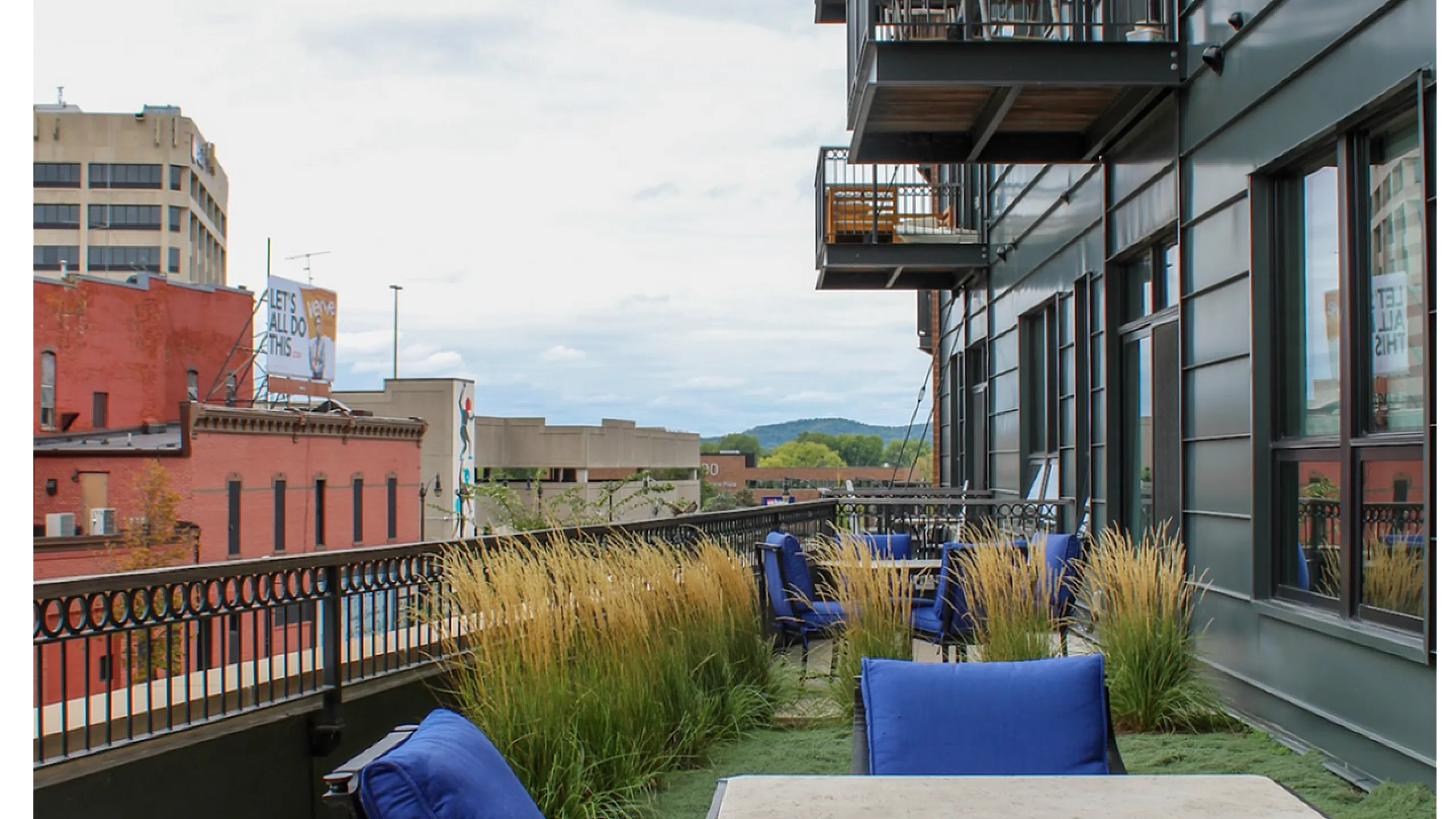 Chic apartment balcony with blue cushioned chairs and lush greenery overlooking cityscape.