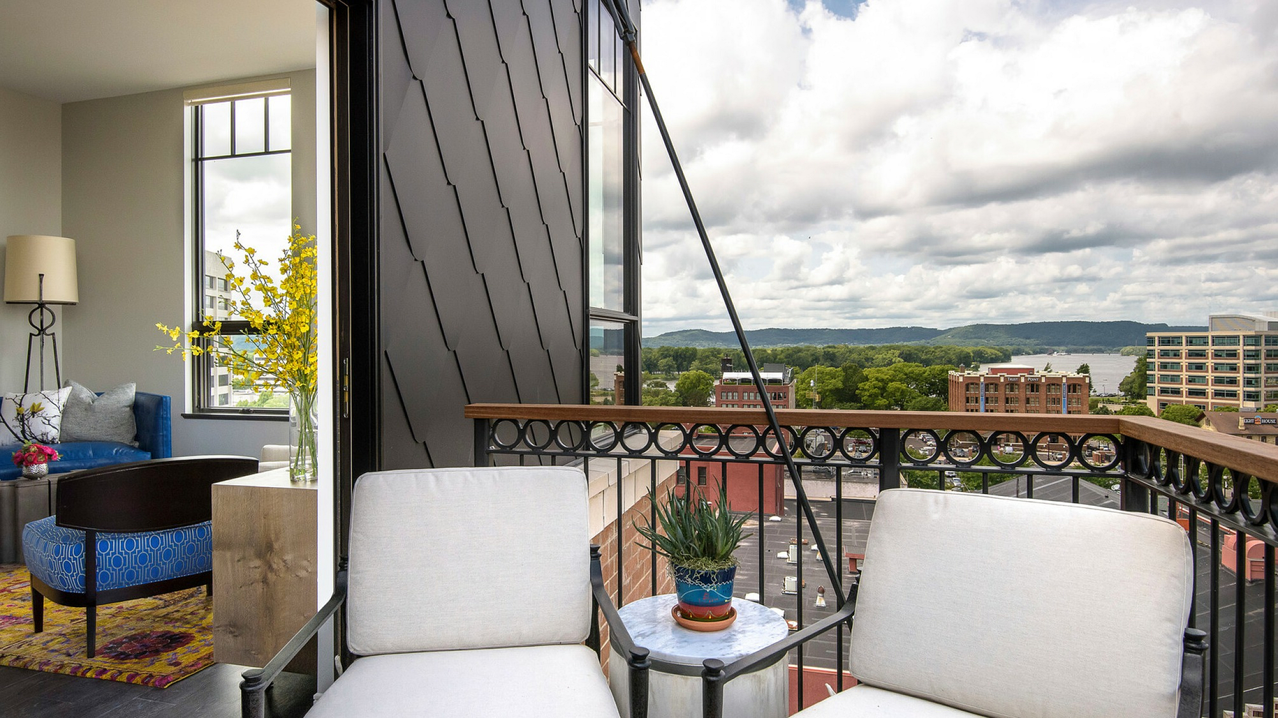 Elegant apartment balcony with comfortable seating overlooking a vibrant cityscape and lush greenery.