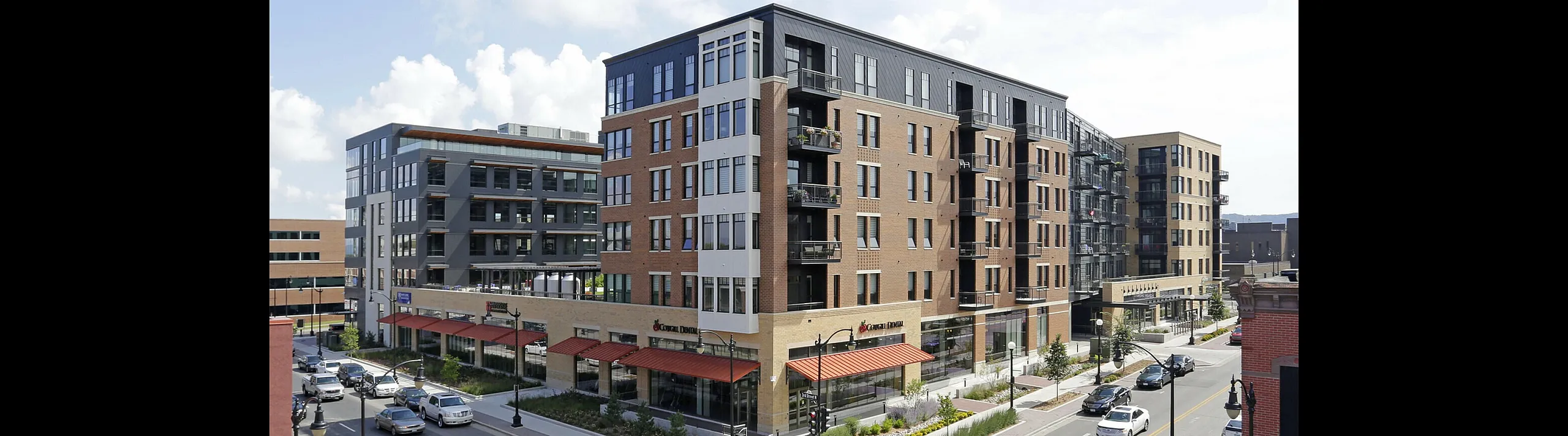 Modern apartment building with multiple floors, large windows, and street-level shops in an urban setting.