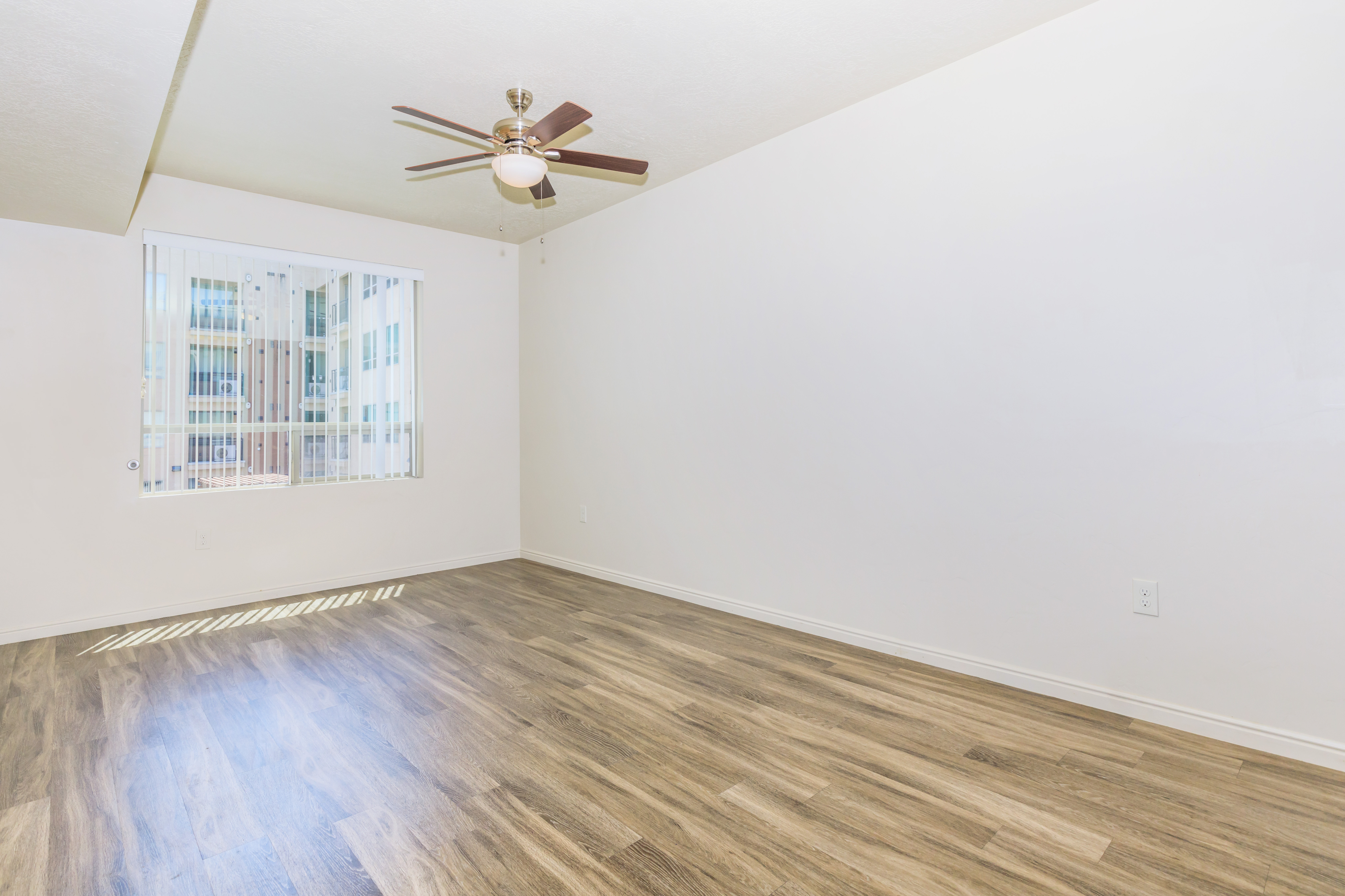 Bright and spacious room with elegant wood flooring and a modern ceiling fan, enhanced by natural light through large windows.