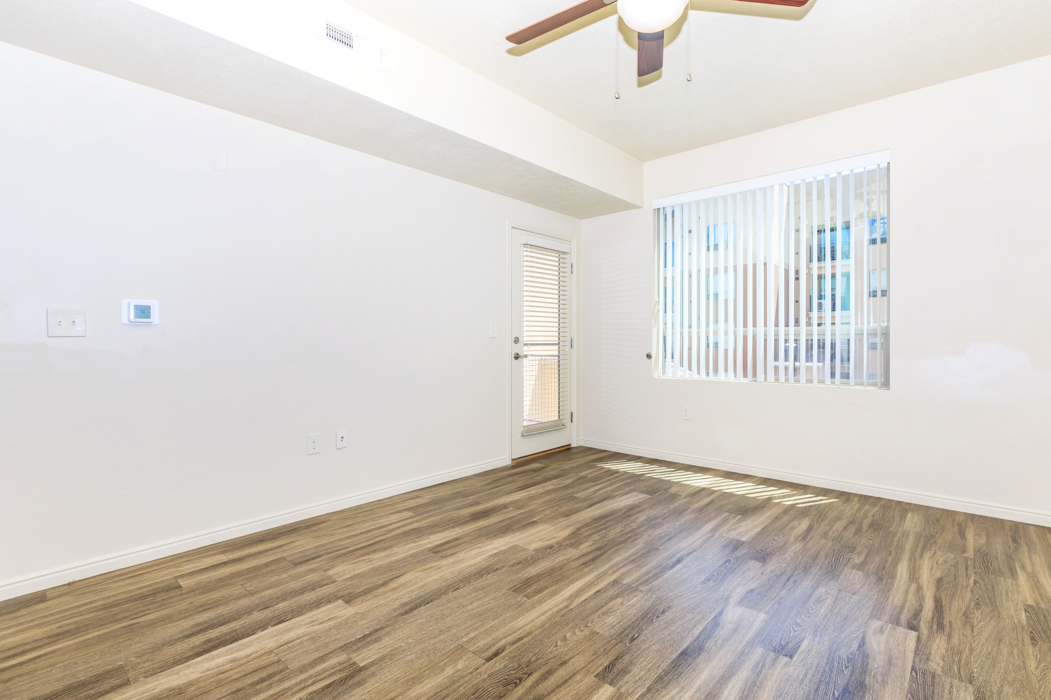 Bright and airy room with wood-style flooring, large window blinds, and a ceiling fan, perfect for a modern living space.