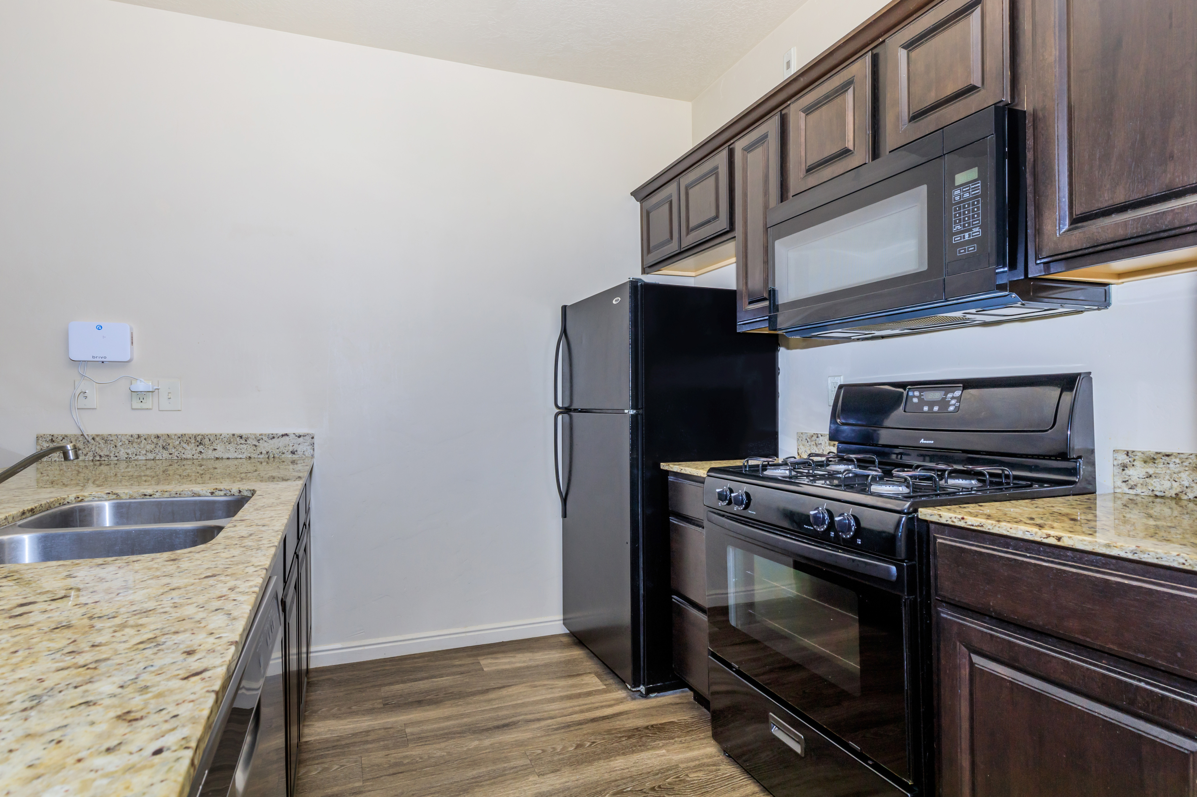 Modern kitchen featuring sleek granite countertops, dark wood cabinets, and a stylish black appliance suite, ideal for culinary creativity.
