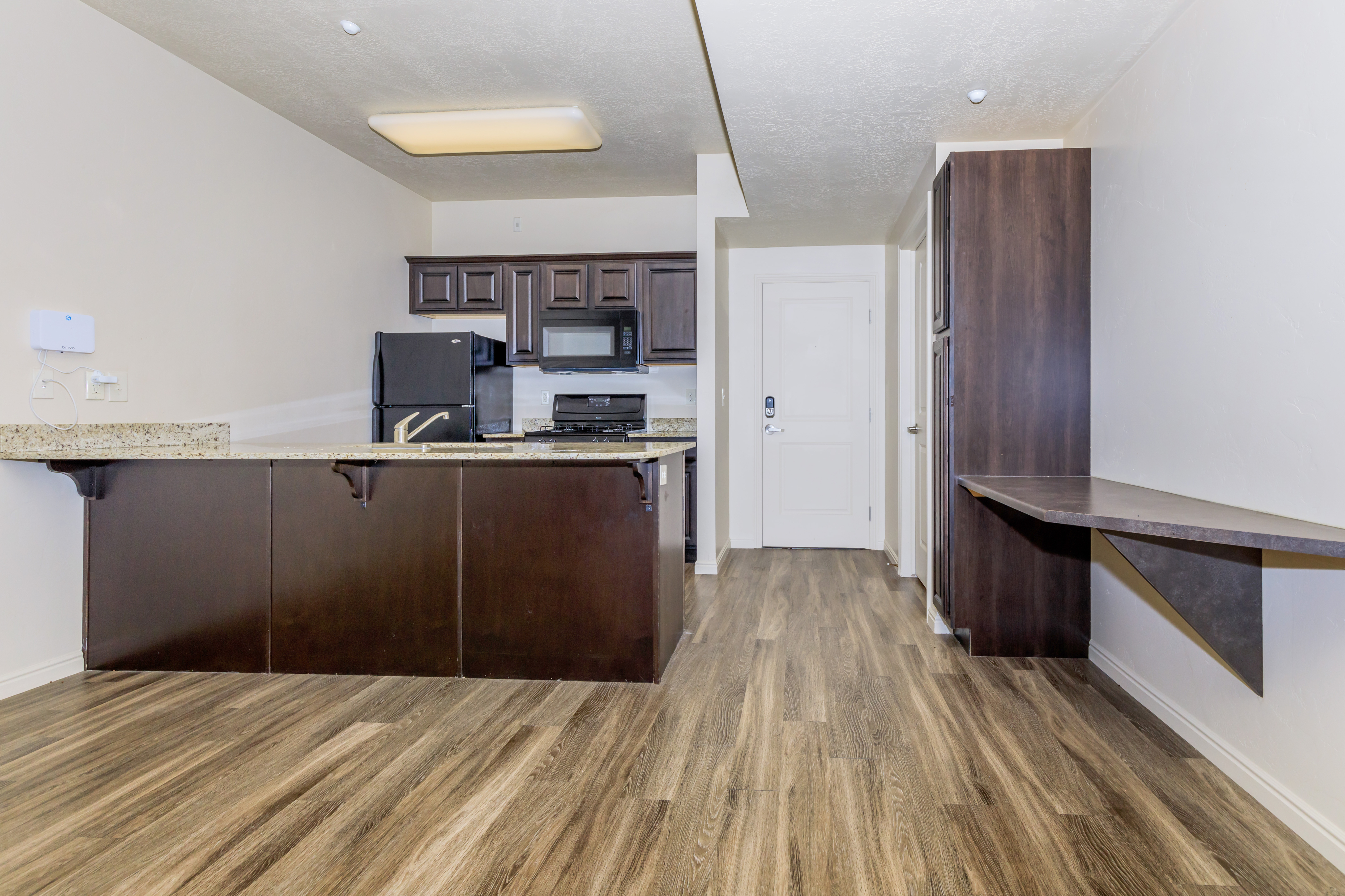 Modern kitchen with sleek dark wood cabinets, granite countertops, and laminate flooring, offering a stylish and functional space.