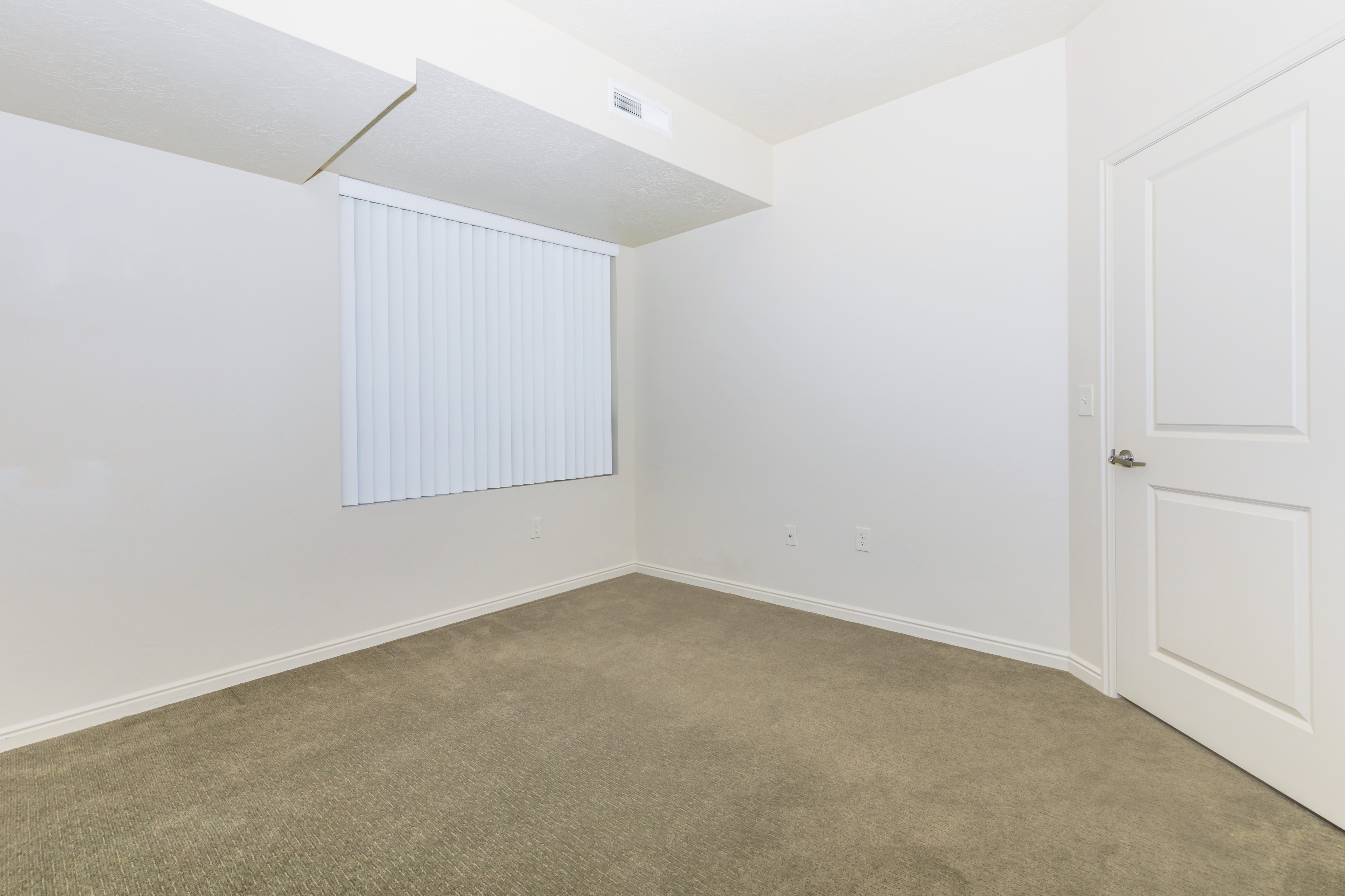 Pristine empty room with plush carpeting, sleek white walls, and modern window blinds, offering a blank canvas for personalization.