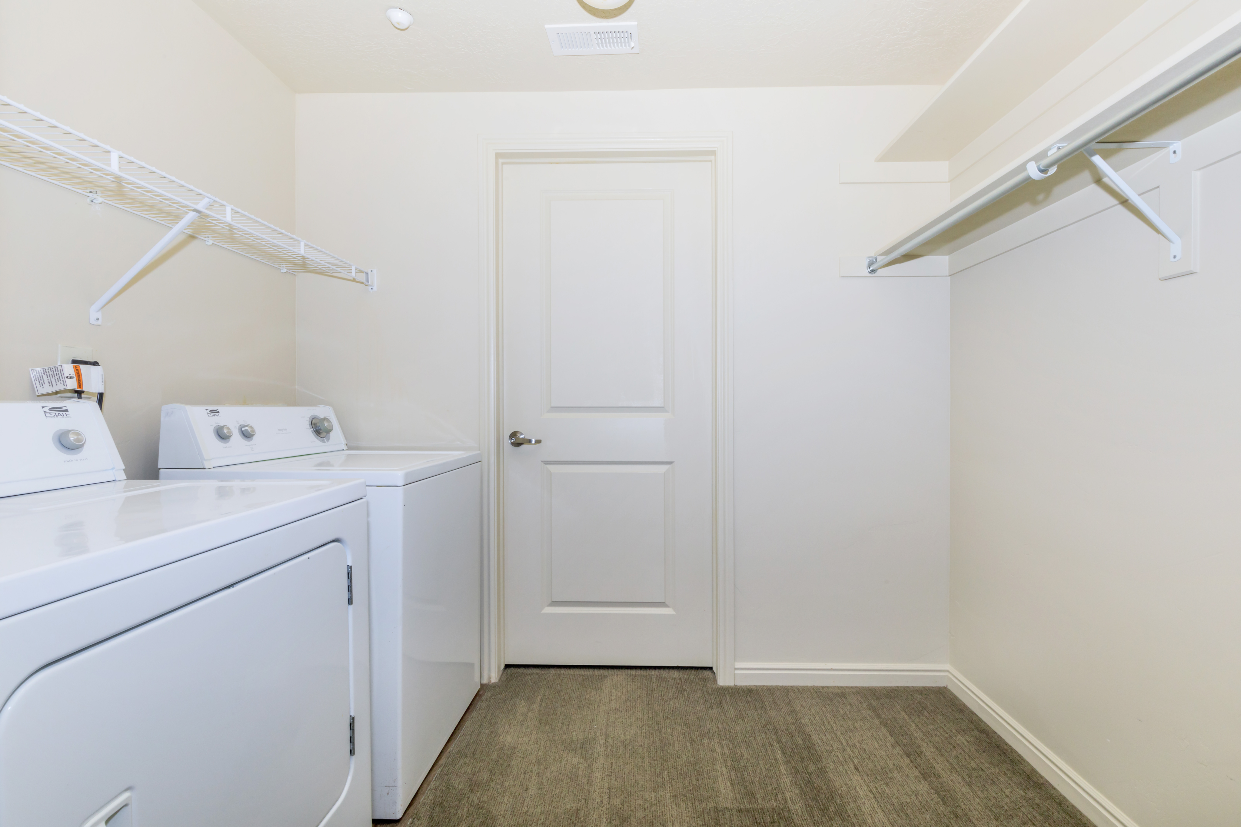 Bright and spacious laundry room with modern washer and dryer, ample shelving, and sleek carpeting.