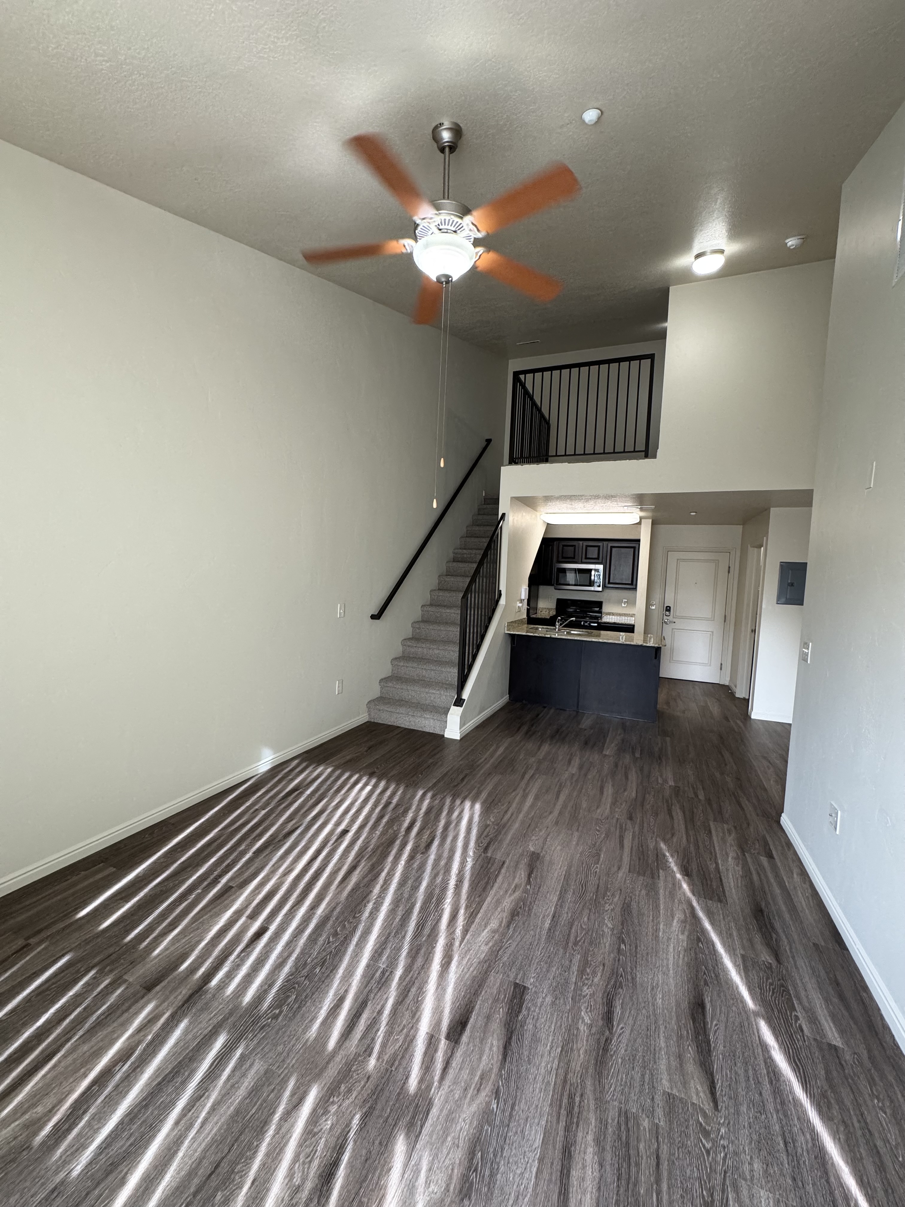 Chic loft apartment with high ceilings, ceiling fan, modern kitchen, and elegant wooden floors.