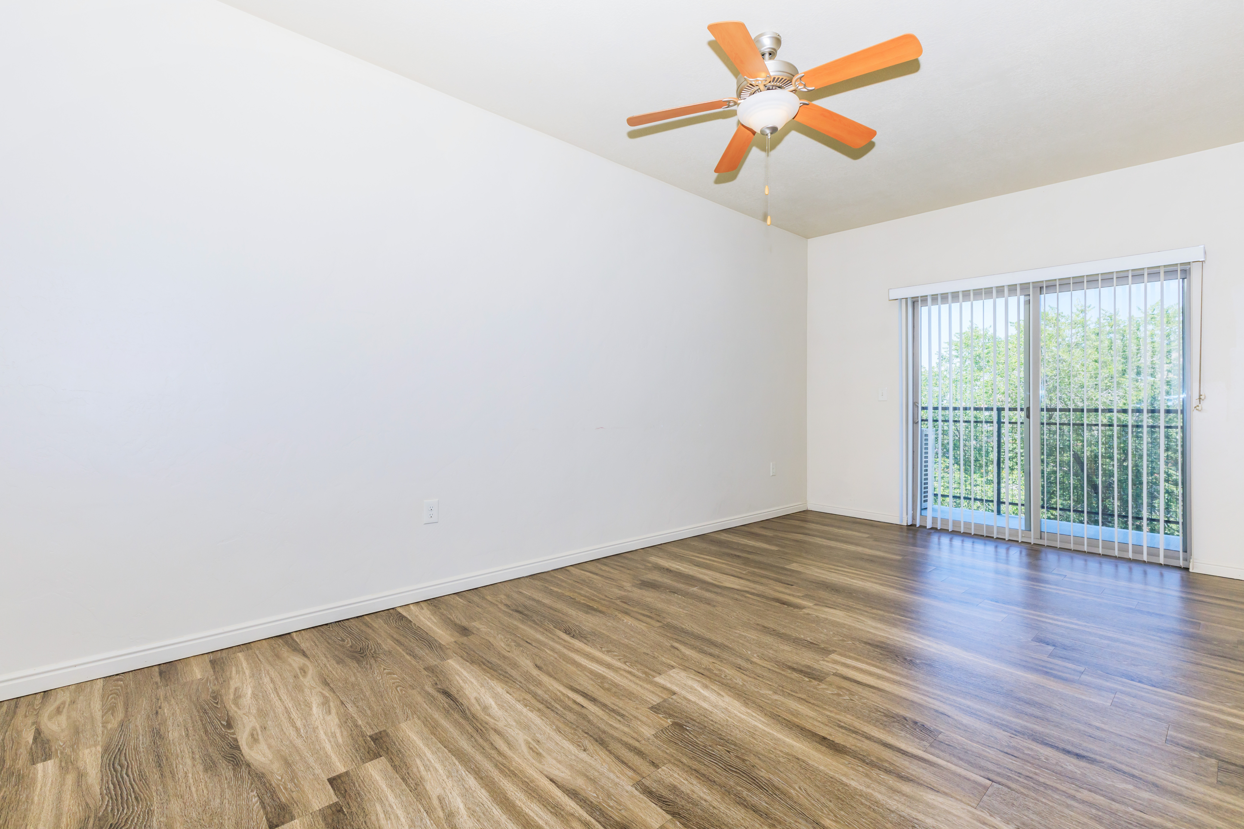 Bright spacious room with elegant wood flooring, ceiling fan, and large sliding glass door opening to scenic views.