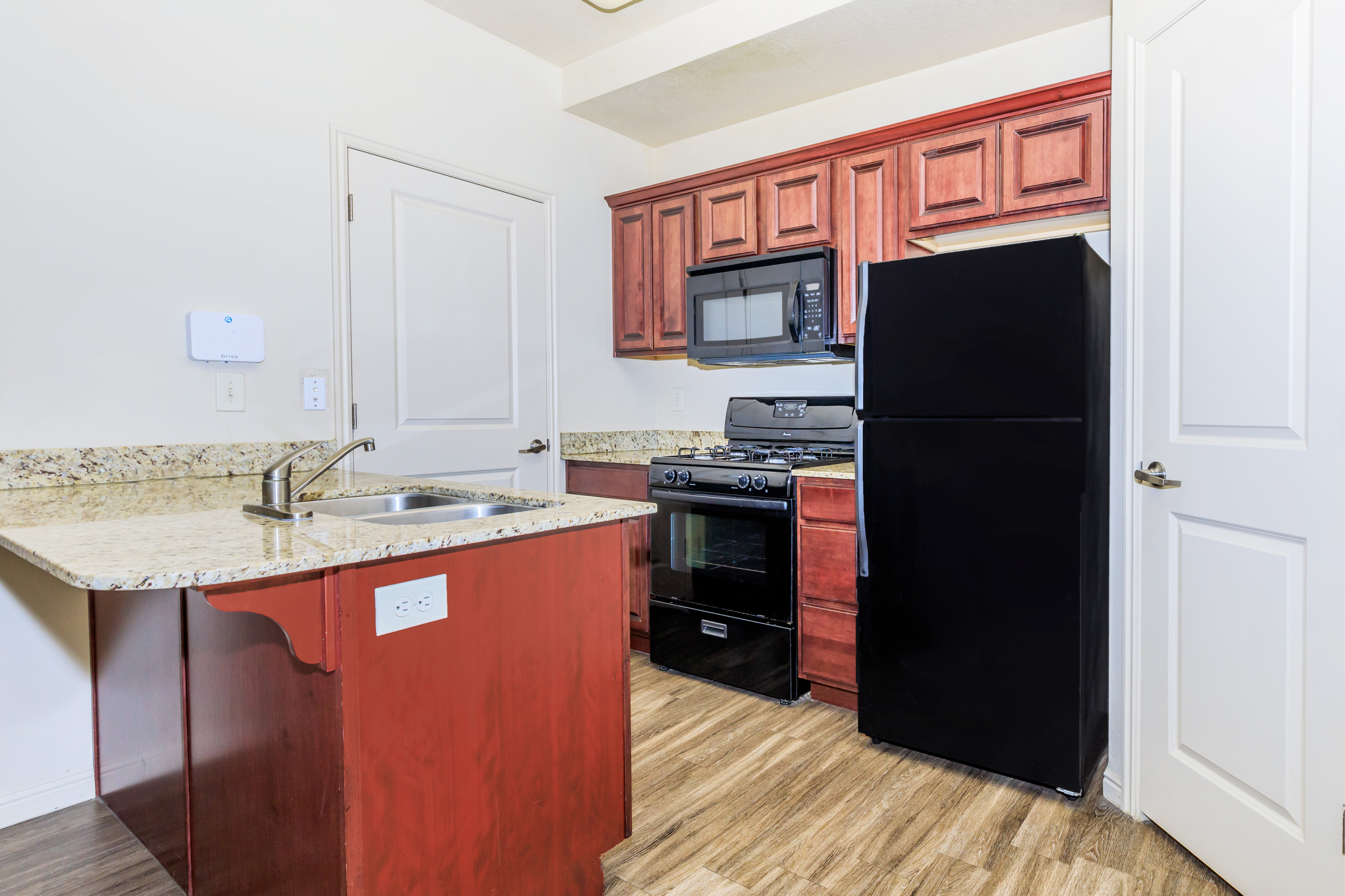 Modern kitchen with elegant granite countertops, rich wooden cabinetry, and sleek black appliances, perfect for culinary enthusiasts.