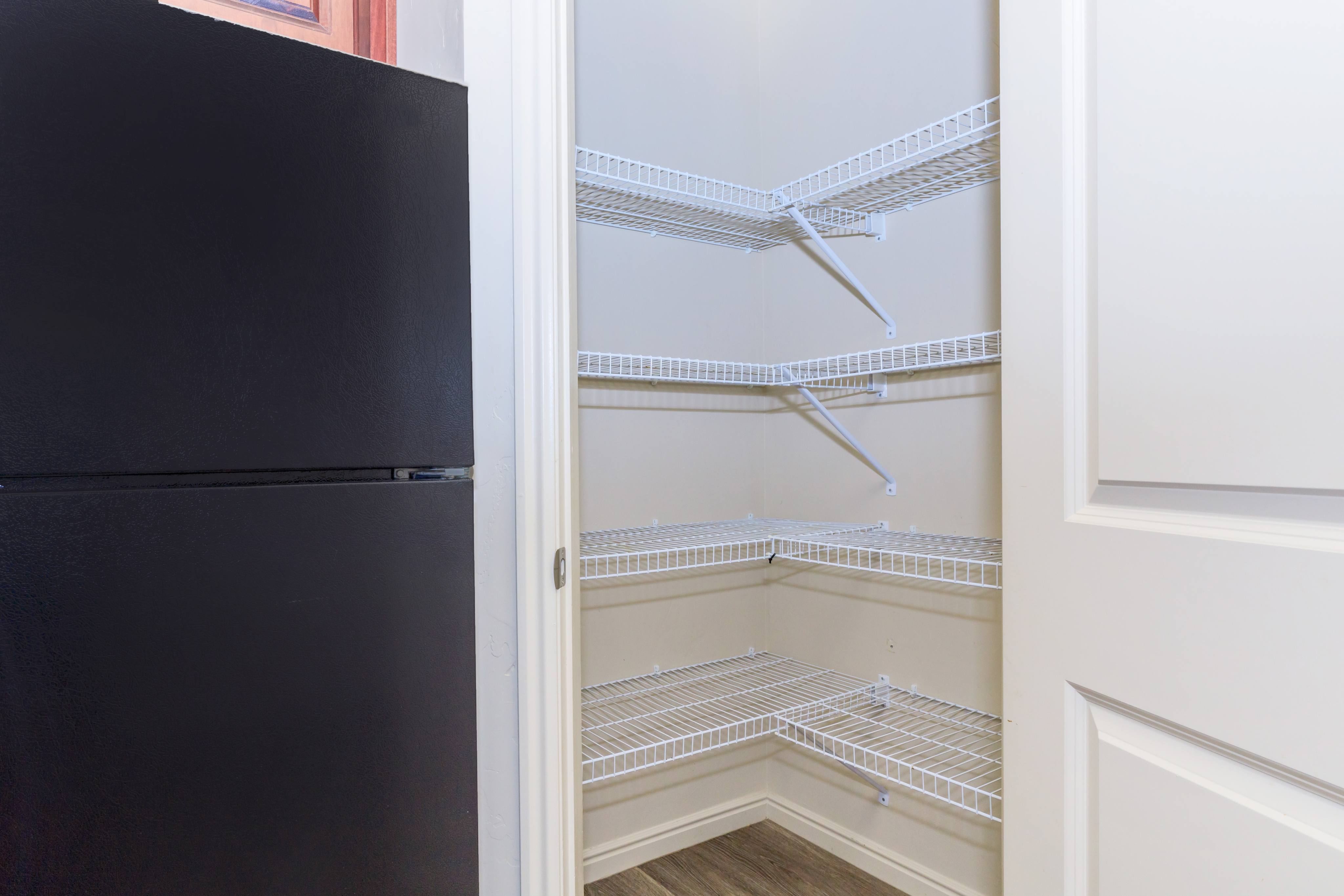 Spacious pantry with sleek white wire shelving next to a modern black refrigerator.