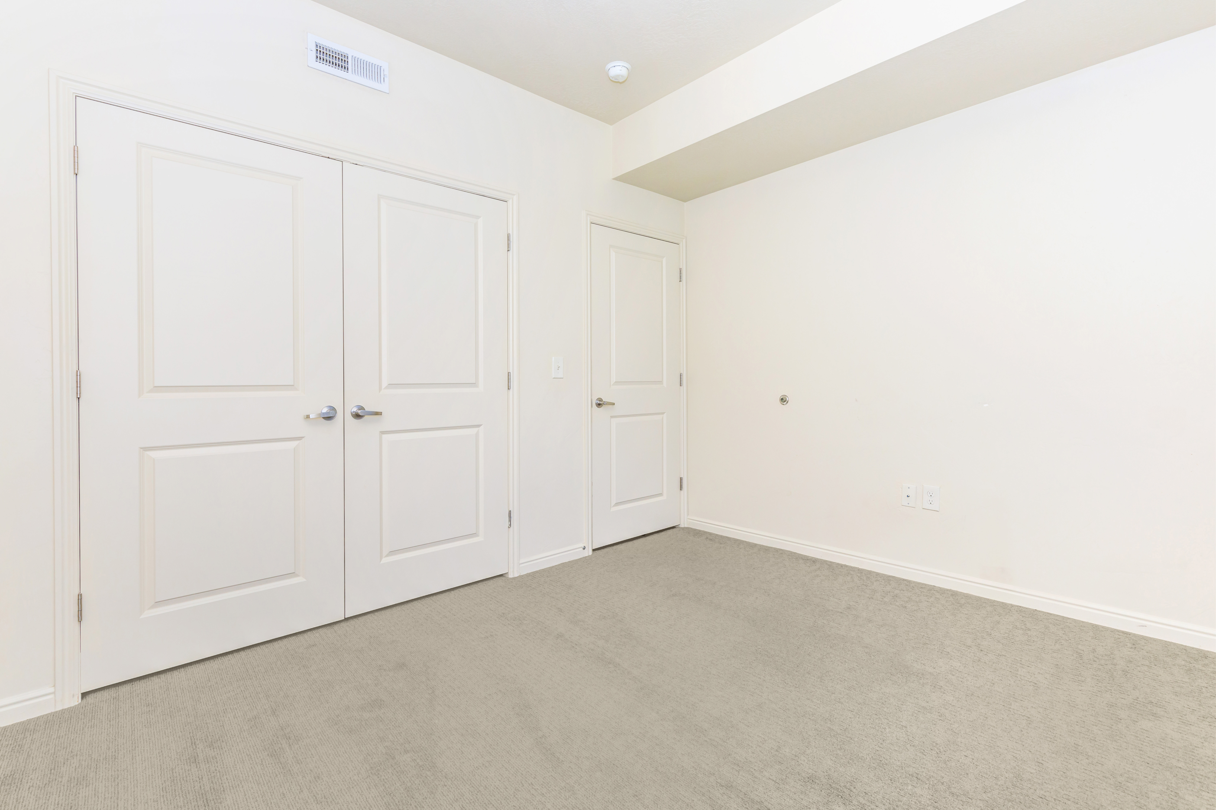 Bright and spacious room with two elegant white doors, plush carpeting, and modern minimalist design.