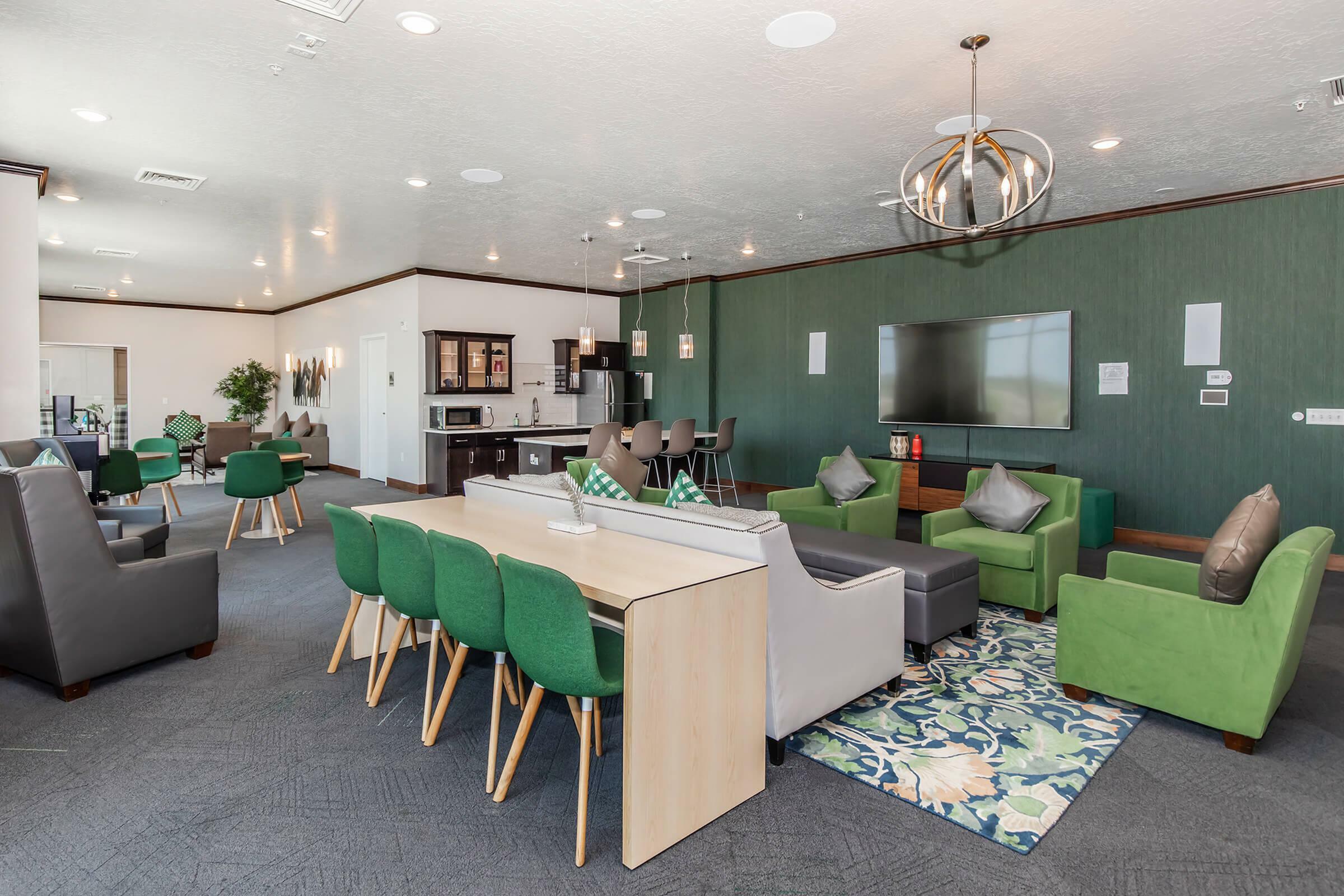 Elegant and modern communal living area featuring stylish green chairs, contemporary lighting, and a sleek open kitchen with bar seating.