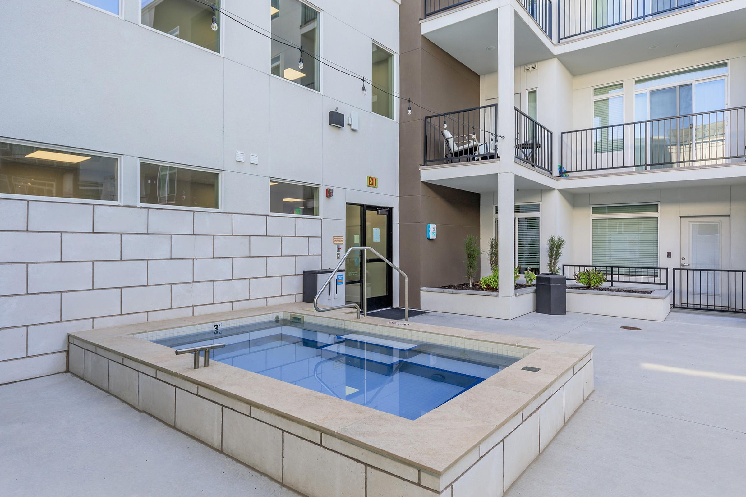 View of a limestone-colored hot tub with bright blue water in the brightly sun-lit courtyard in the center of the community.