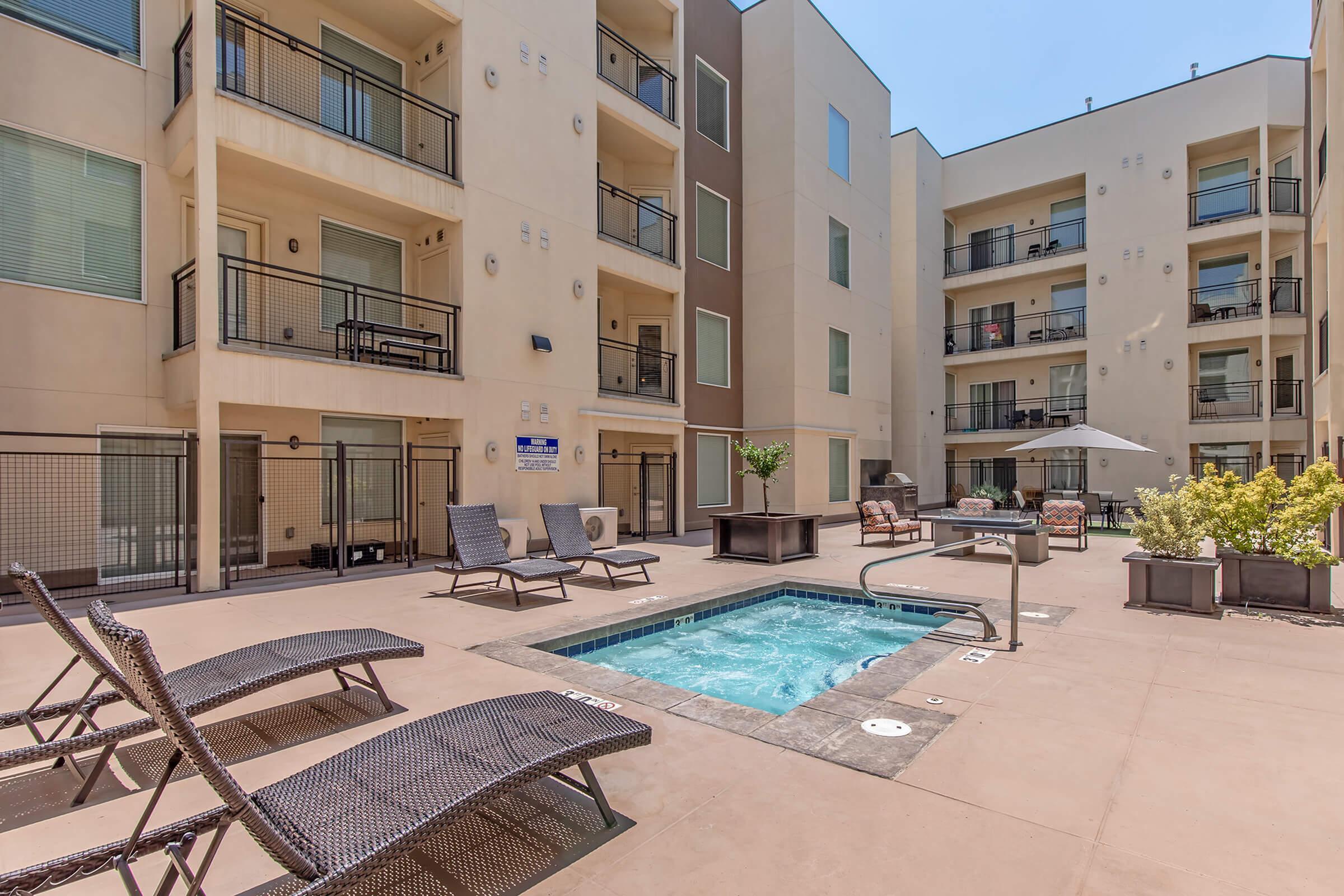 Modern apartment complex courtyard featuring a sleek spa pool surrounded by stylish lounge chairs, perfect for relaxation and socializing.