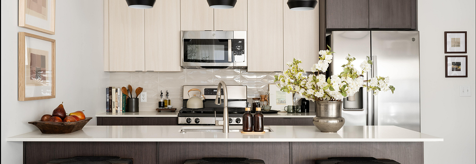 Modern kitchen with sleek appliances, elegant pendant lights, and a stylish breakfast bar adorned with fresh flowers, creating an inviting cooking space.