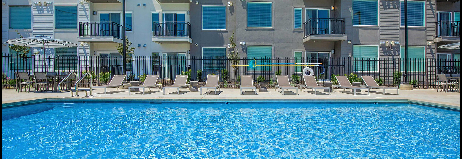 Modern apartment complex featuring sunlit balconies and a luxurious swimming pool with stylish lounge chairs for ultimate relaxation.