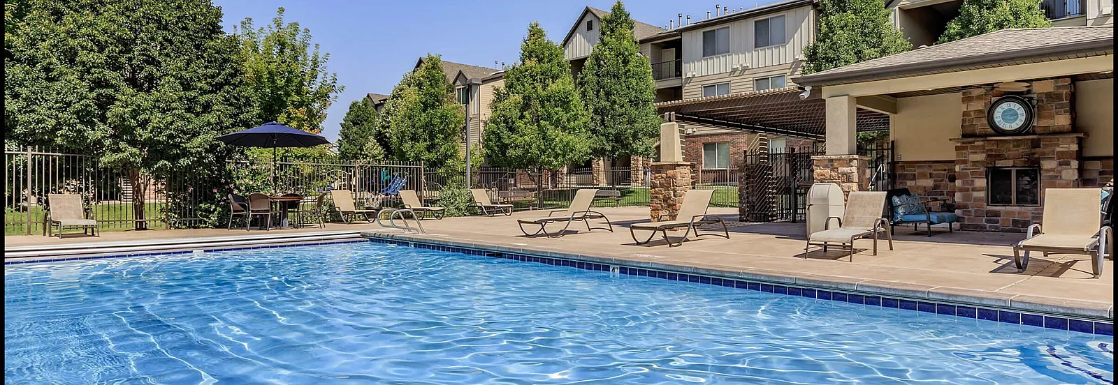 Inviting outdoor pool area with relaxing lounge chairs, lush greenery, and beautifully designed surrounding architecture on a sunny day.
