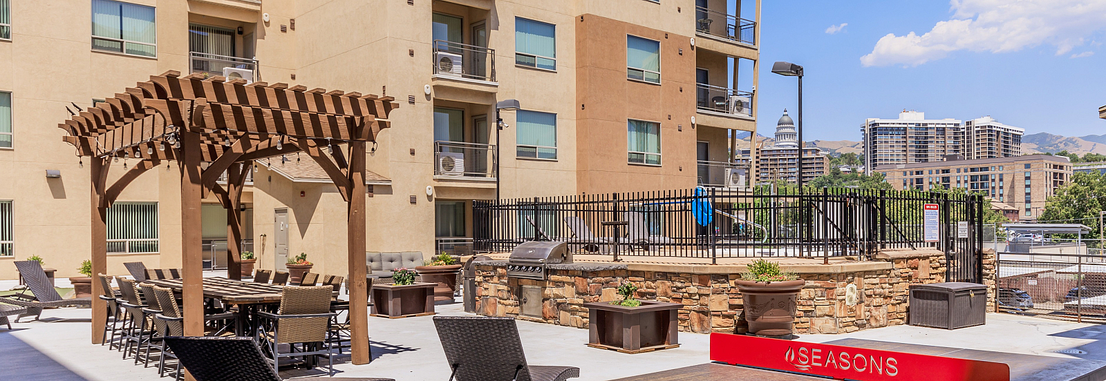 Chic apartment courtyard featuring pergola dining area, sun loungers, and a stylish tennis table, with cityscape views.
