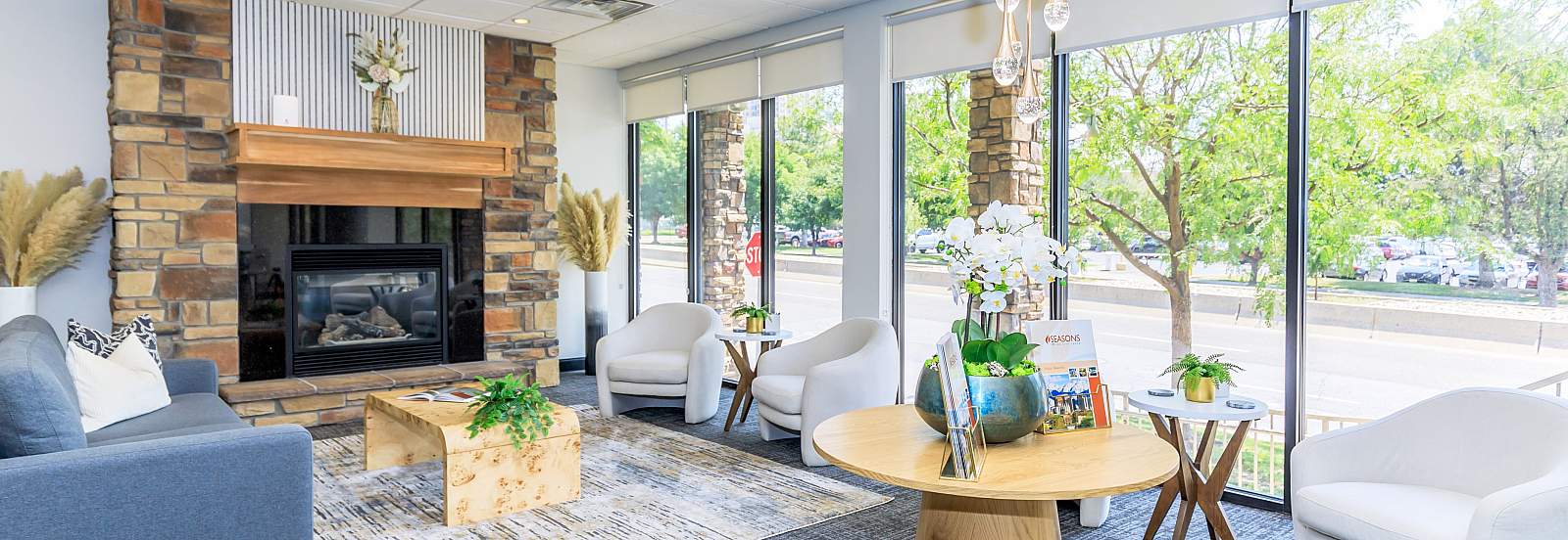 Bright and inviting living space with elegant stone fireplace, modern furniture, and large windows overlooking lush greenery.