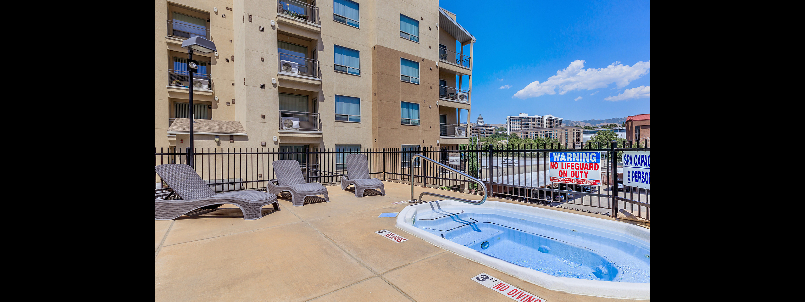 Modern apartment building with relaxing outdoor spa area, featuring comfortable lounge chairs and a stunning city view.