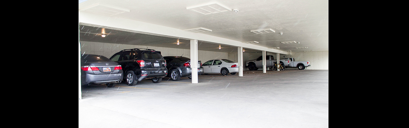 Bright covered parking area featuring multiple sedans and trucks of various colors.