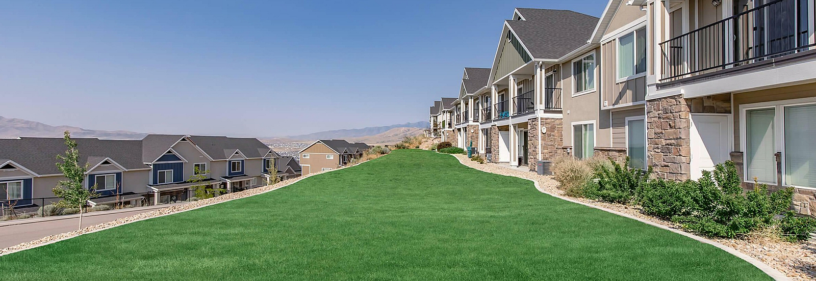 Charming residential community featuring stylish townhouses with spacious balconies, set against a serene landscape and clear blue sky.