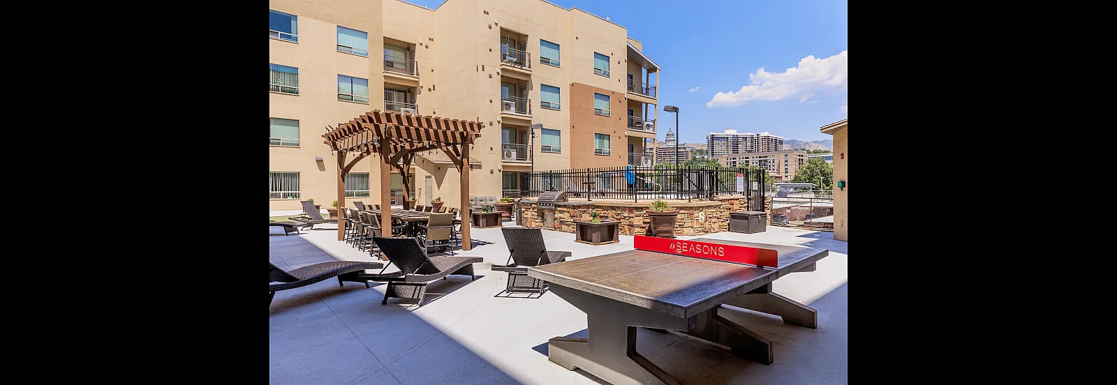 Chic apartment courtyard with stylish loungers, shaded dining area, and city views, perfect for relaxation and entertainment.