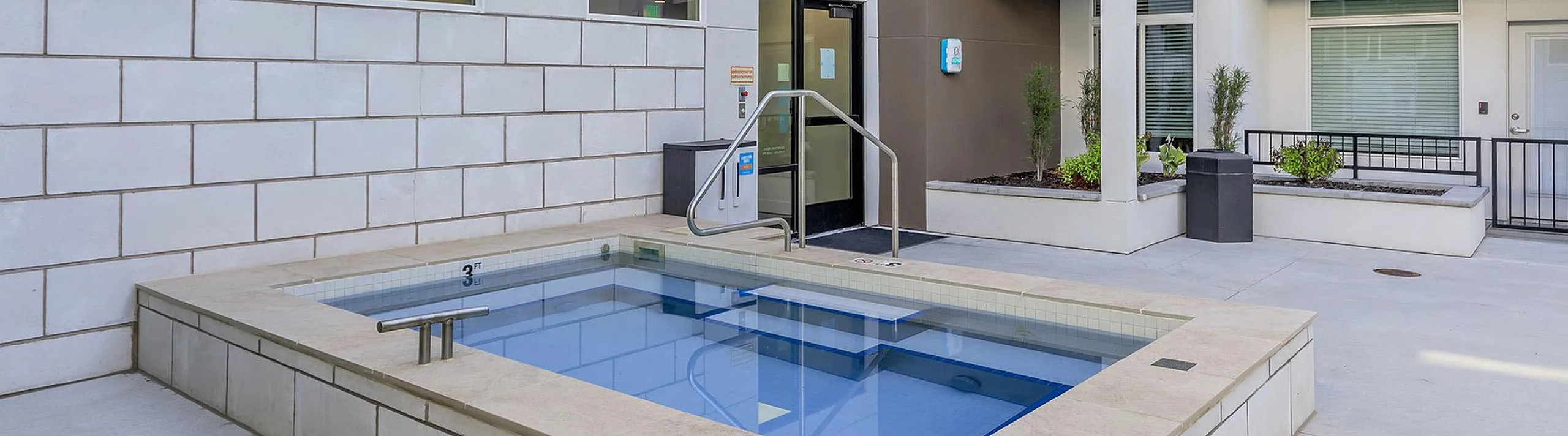 Outdoor year-round hot tub spa at Seasons on Mill Creek featuring stone tile coping, entry handrails, surrounding patio deck, and landscaped planters.