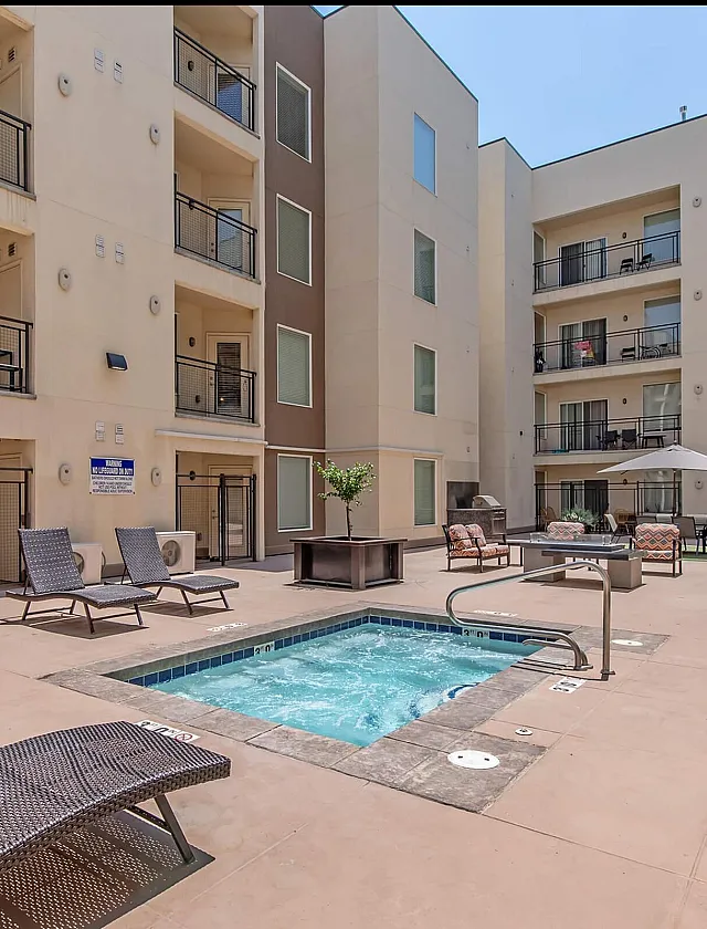 Modern apartment complex featuring a sunlit courtyard with loungers, a relaxing jacuzzi, and stylish balconies.