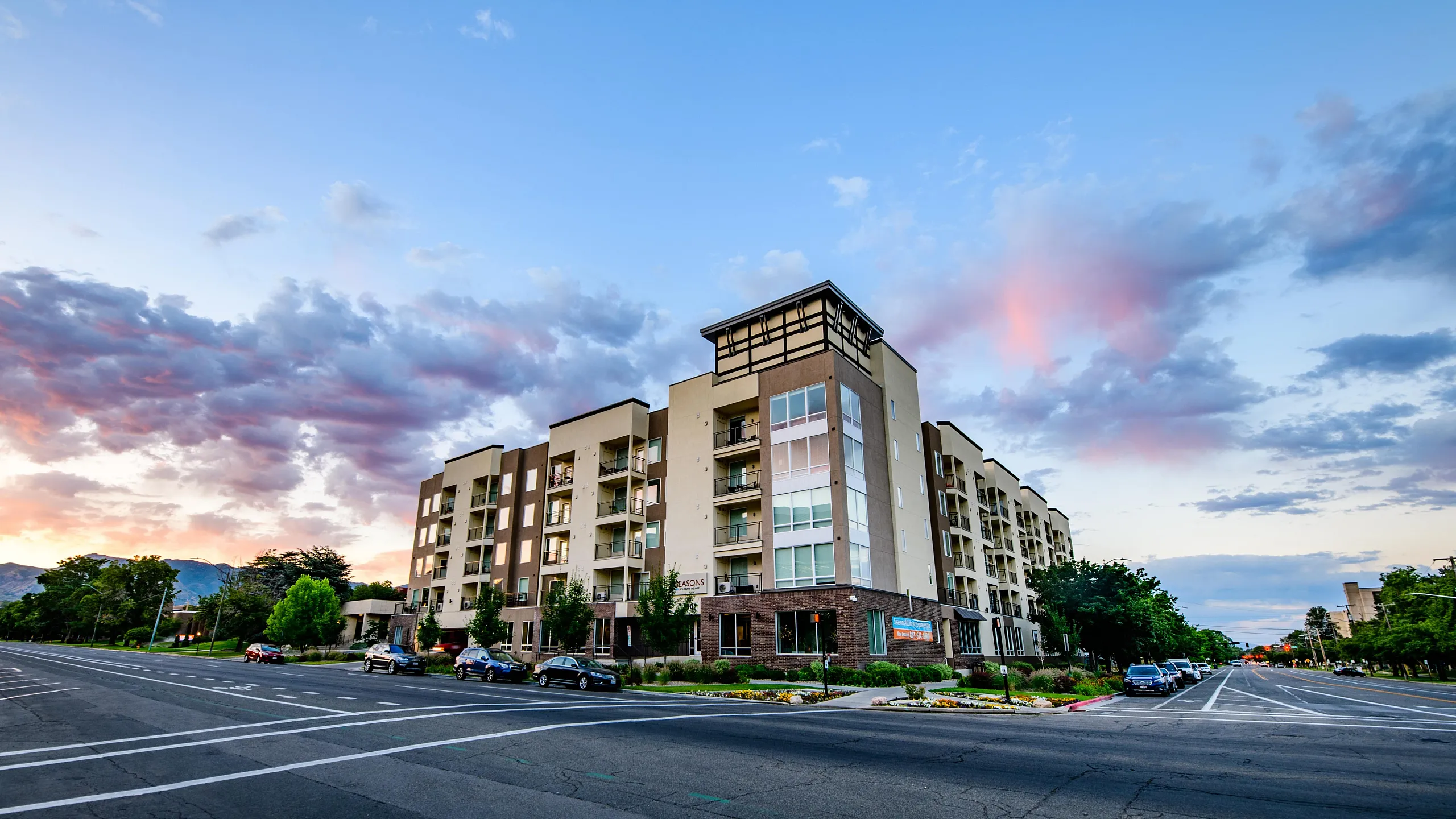 Modern apartment building with large balconies and stylish architecture, set against a vibrant sunset sky.