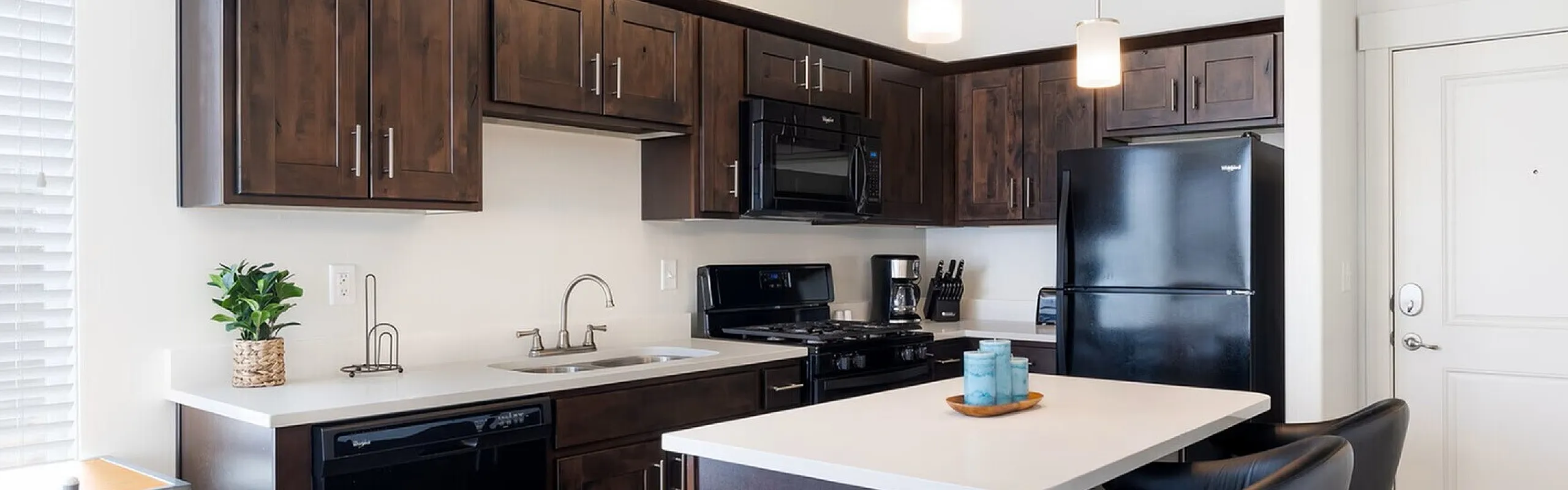 Modern kitchen with sleek dark wood cabinets, black appliances, and a chic island, illuminated by stylish pendant lights.
