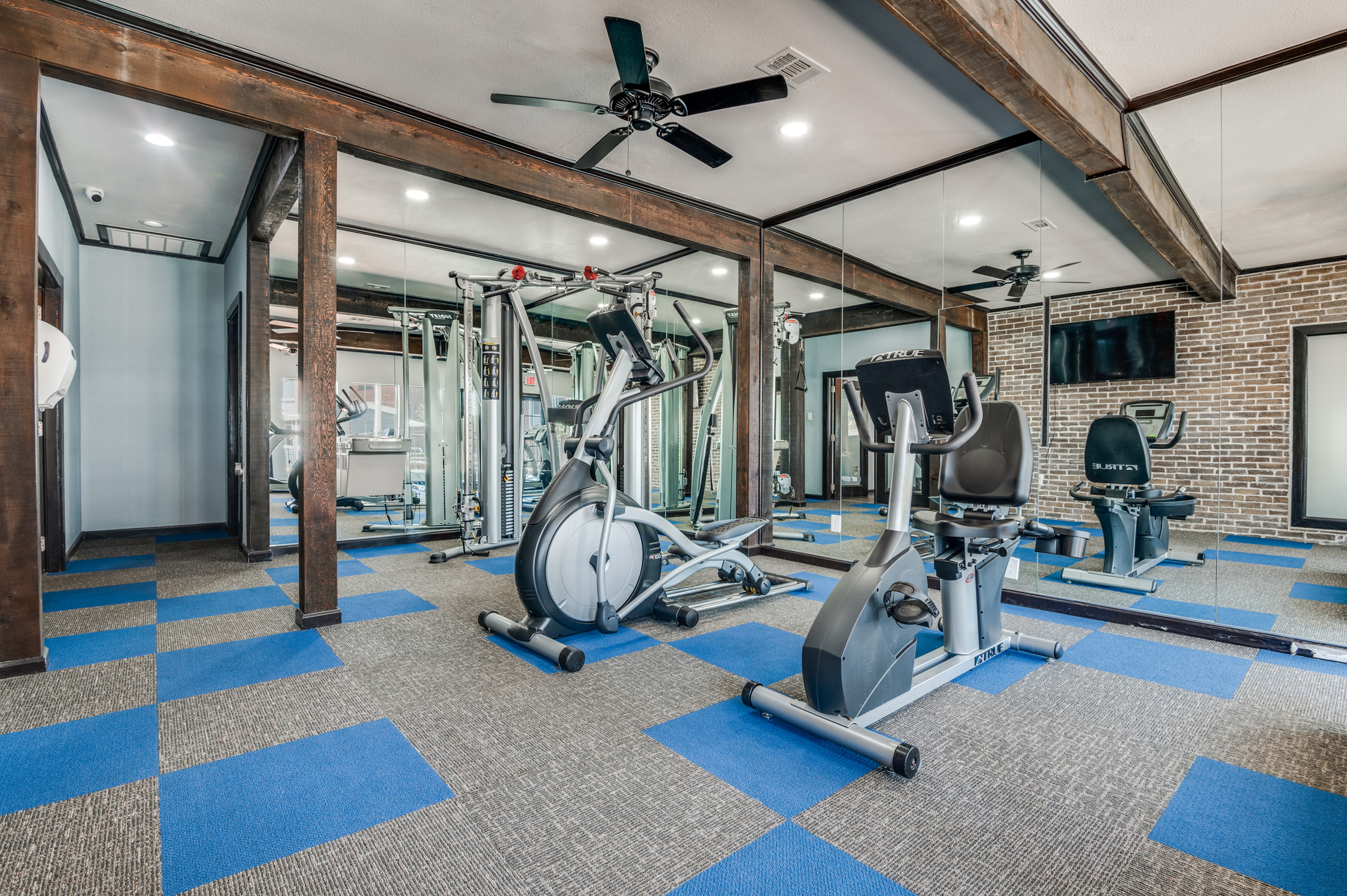 Modern fitness room with sleek exercise equipment, mirrored walls, and stylish blue-accented flooring for an energizing workout experience.