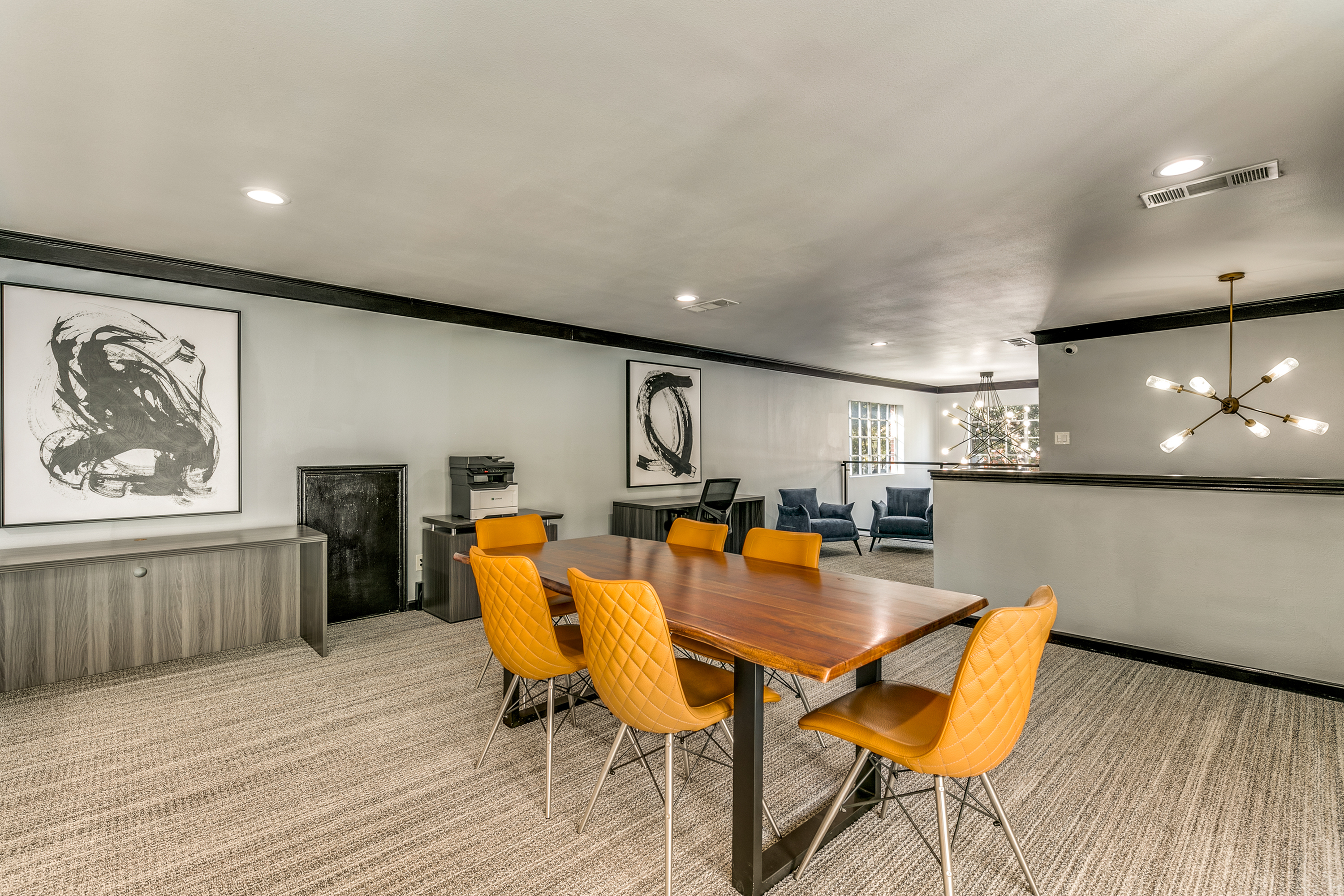 Elegant conference room with modern decor, featuring a sleek wooden table and vibrant orange chairs, highlighted by contemporary artwork and chic lighting.