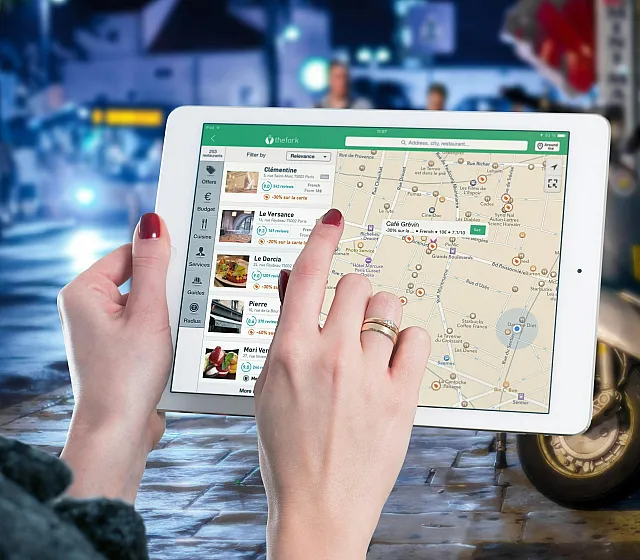 Hands holding a tablet displaying a city map with nearby dining options, set against a vibrant urban night scene.
