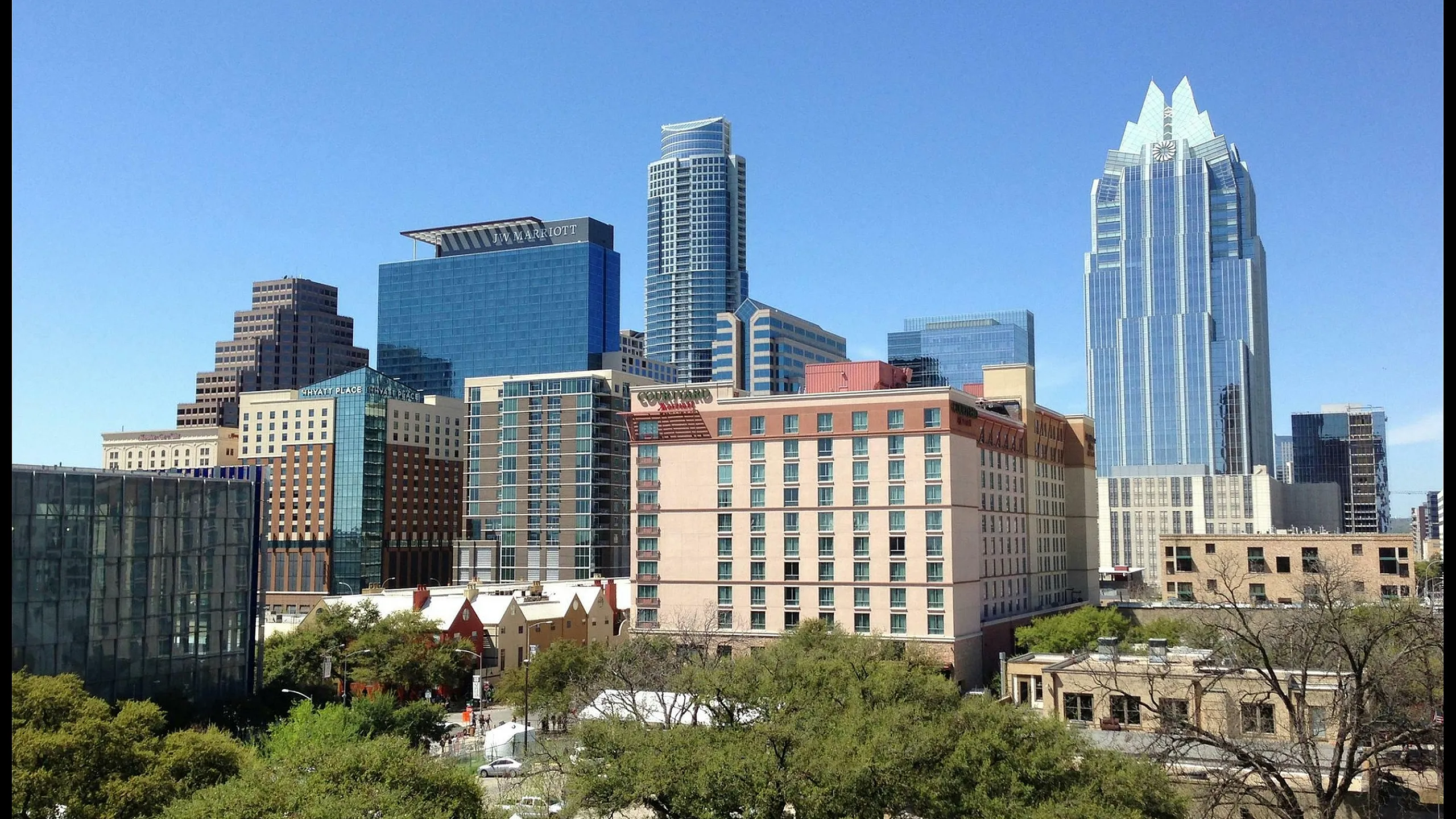 Captivating city skyline featuring modern skyscrapers under a clear blue sky, surrounded by lush greenery.