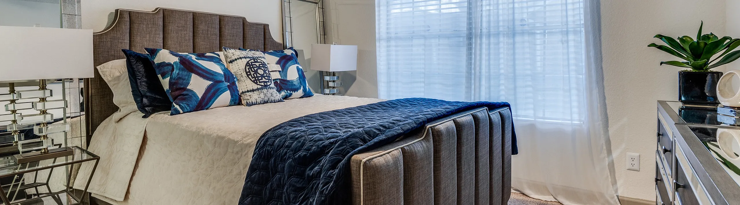 Elegant bedroom with plush bedding, modern decor, and abundant natural light from large window.