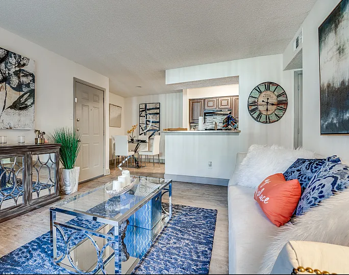 Chic open-plan living room with contemporary decor, featuring a stylish glass coffee table, elegant dining area, and modern kitchen in a warm, inviting space.